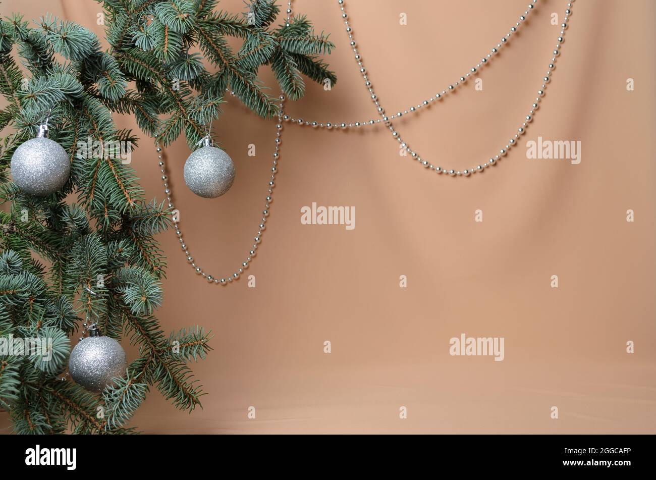 Decorazione di Capodanno. Rami di abete rosso con palline d'argento su sfondo beige ondulato in chiffon. Messa a fuoco selettiva. Foto Stock