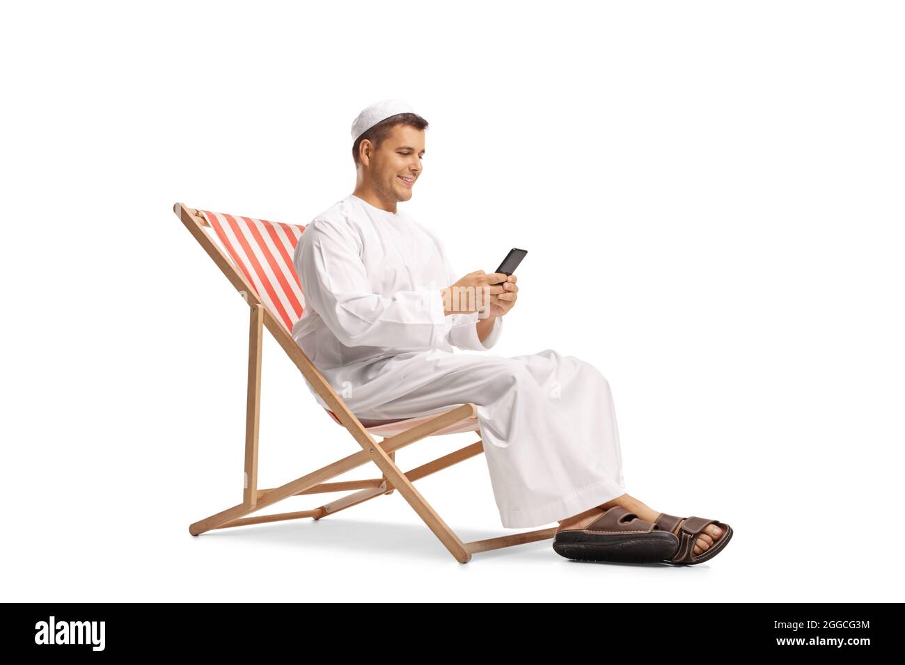 Giovane uomo in abiti etnici seduto su una sedia da spiaggia con un telefono cellulare isolato su sfondo bianco Foto Stock