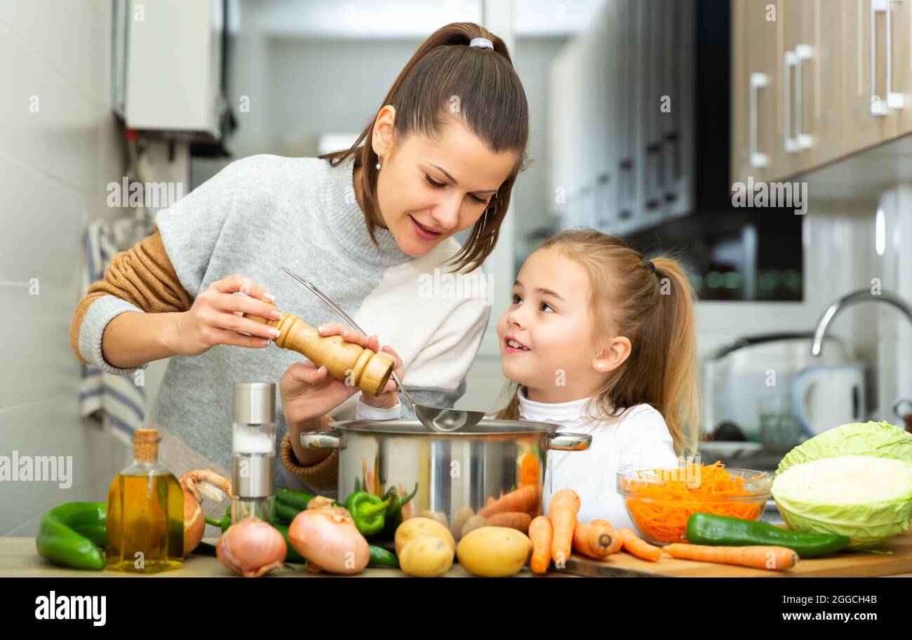 La figlia che aiuta a cucinare la zuppa e la madre aggiungono il pepe alla padella Foto Stock