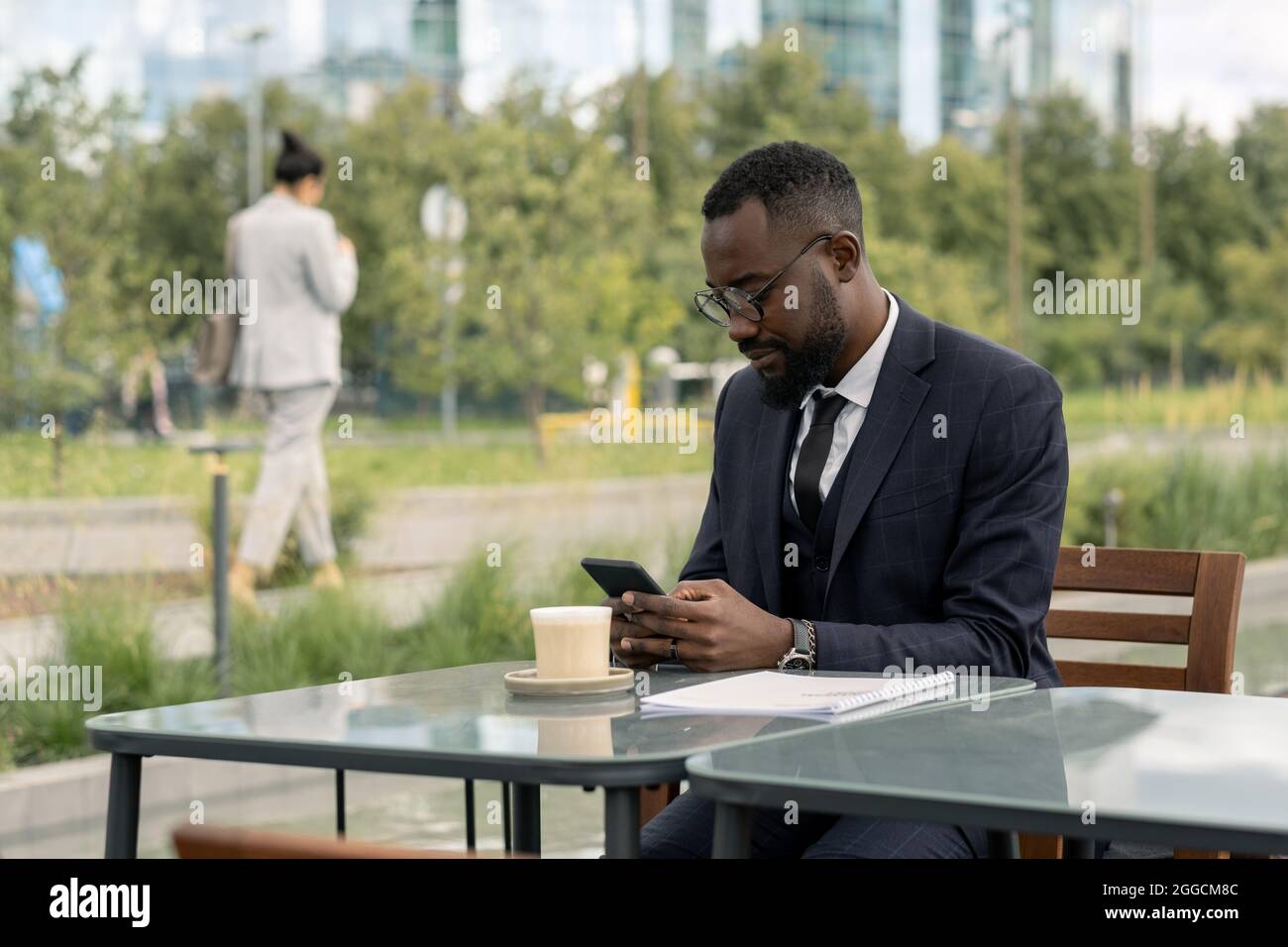 Serio uomo d'affari africano con smartphone testing al tavolo in un bar all'aperto Foto Stock