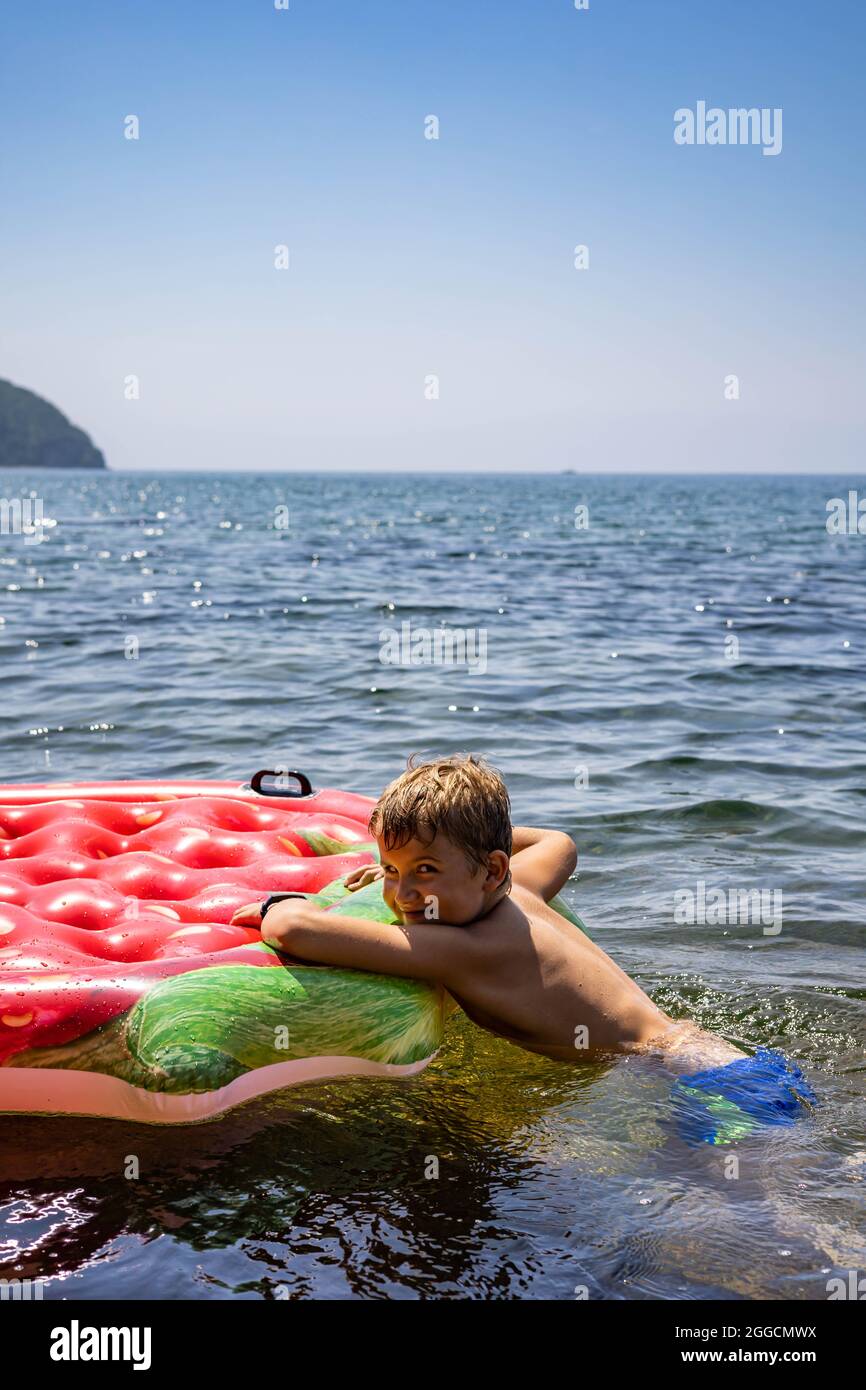 Divertente ragazzo di capretto che galleggia su gomma gonfiabile Strawberry  salvagente circondato da acqua di mare pura e limpida Foto stock - Alamy