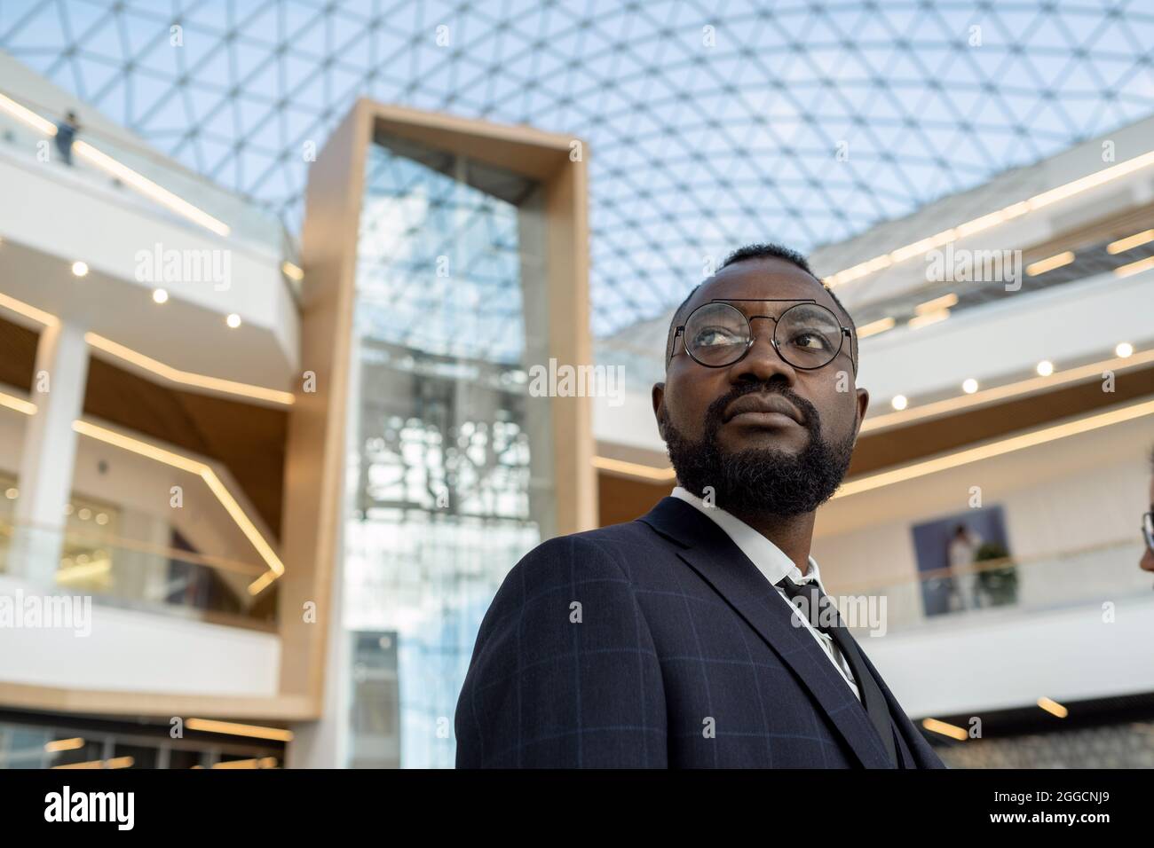 Giovane uomo d'affari africano serio che guarda in avanti e che si oppone all'architettura moderna Foto Stock