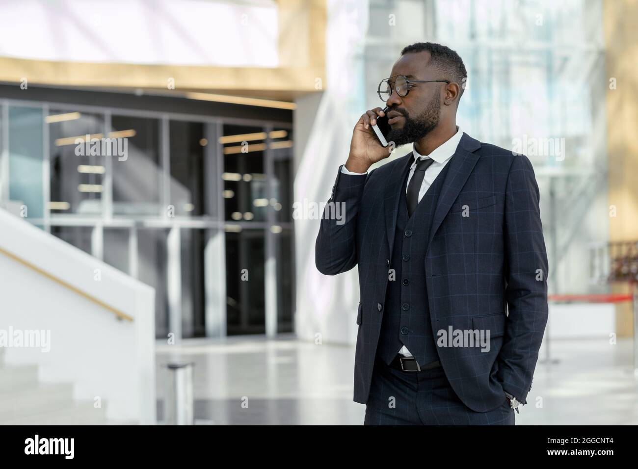 Giovane ed elegante uomo d'affari che comunica con il telefono cellulare mentre si trova in un moderno centro affari Foto Stock