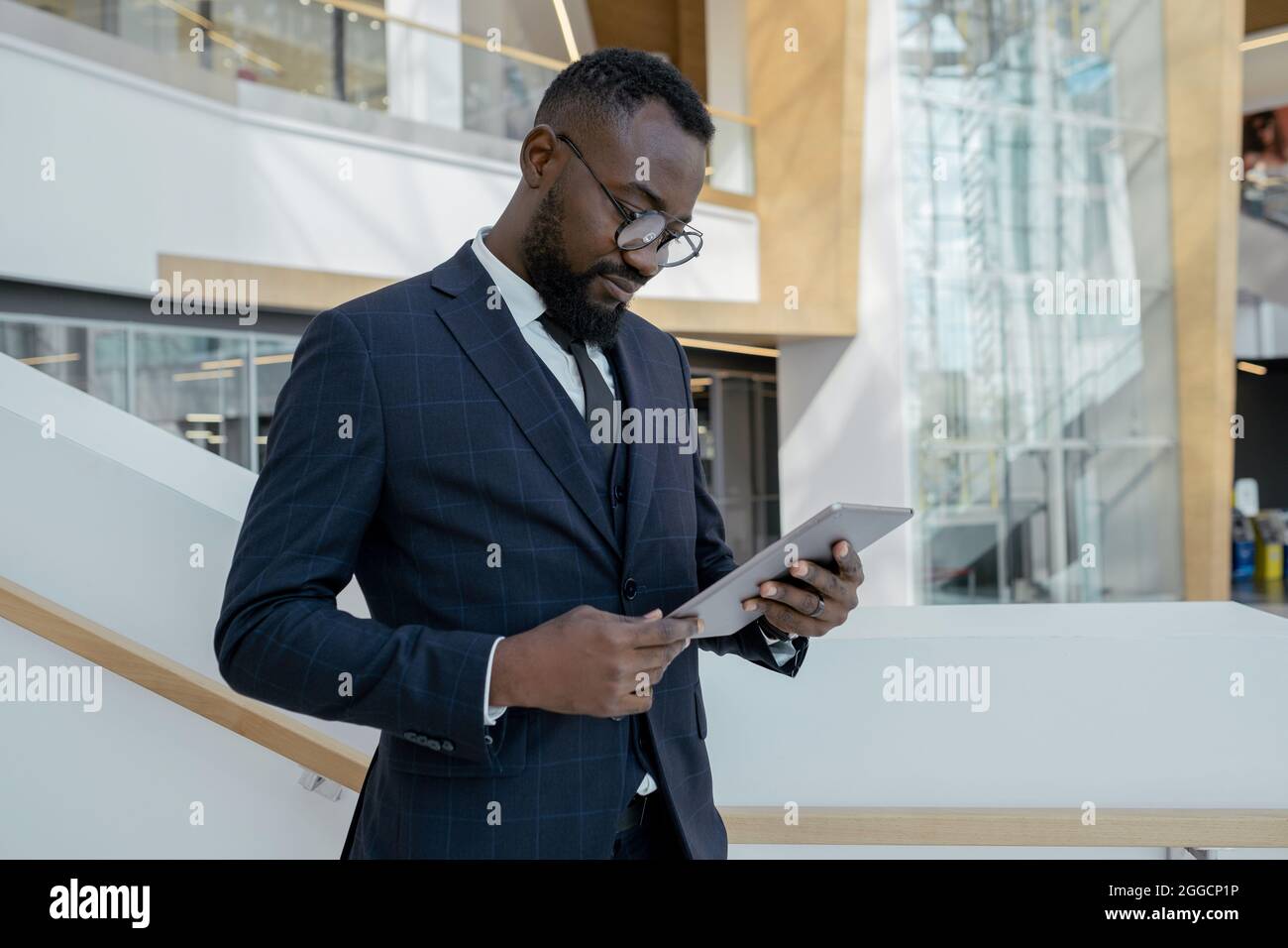Giovane uomo d'affari che guarda le notizie online sul display del tablet mentre si trova in un ampio business center Foto Stock