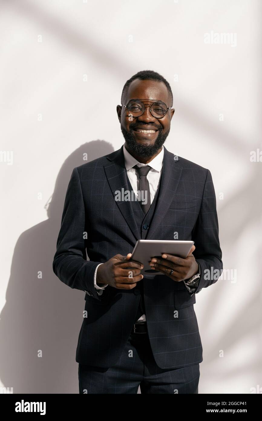 Uomo d'affari di successo in un abito elegante che ti guarda con un sorriso mentre usi il tablet Foto Stock