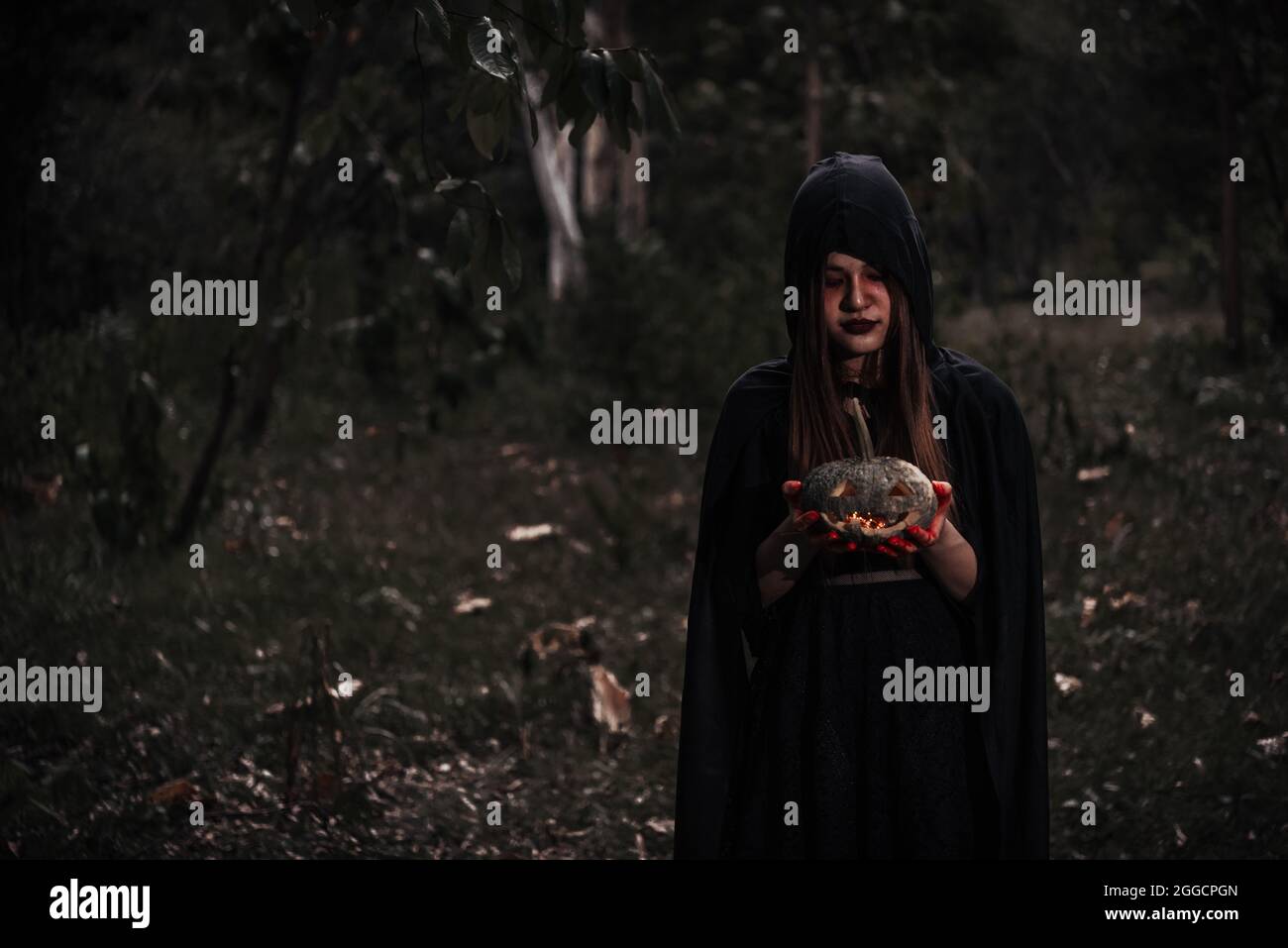 Donna horror fantasma che tiene il reaper e zucca inn foresta, halloween concetto Foto Stock