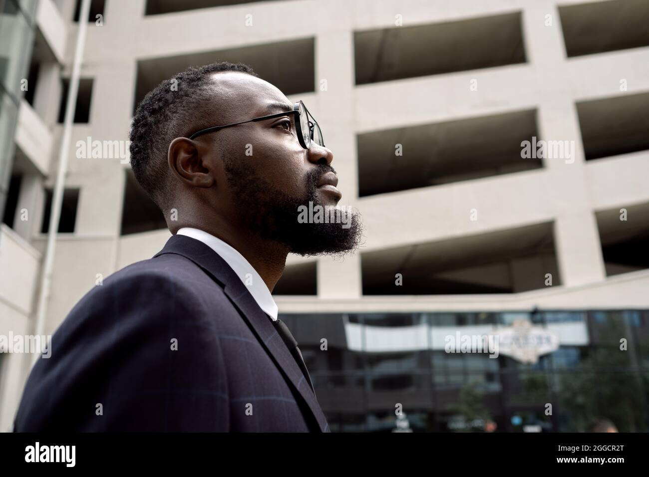Vista laterale di un giovane uomo d'affari serio di etnia africana che si oppone all'architettura moderna Foto Stock