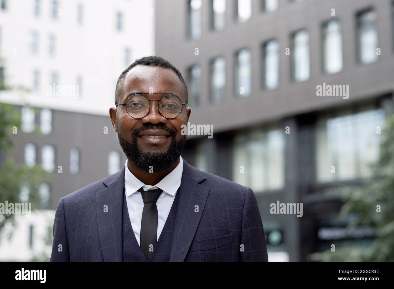 Felice giovane uomo d'affari africano in piedi davanti alla macchina fotografica in ambiente urbano Foto Stock