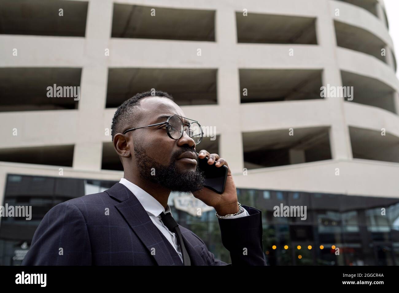 Un giovane uomo d'affari africano serio che tiene lo smartphone all'orecchio mentre si trova contro l'esterno dell'edificio Foto Stock