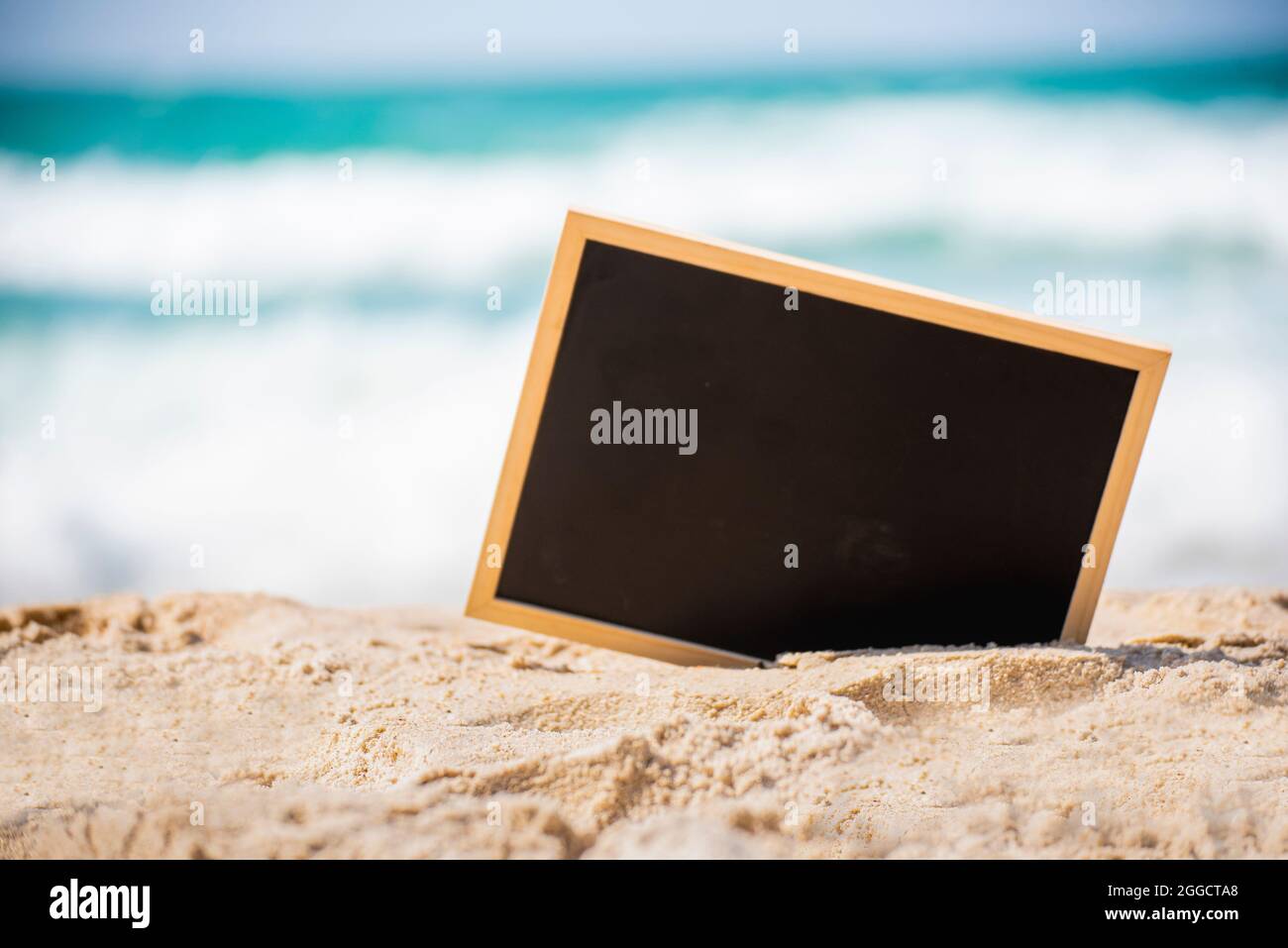 Lavagna vuota sulla spiaggia di sabbia tropicale estiva con cornice in legno per visualizzare il testo. Design del display per il concetto di agenzia di viaggi. Bordo nero vuoto su sabbia c Foto Stock