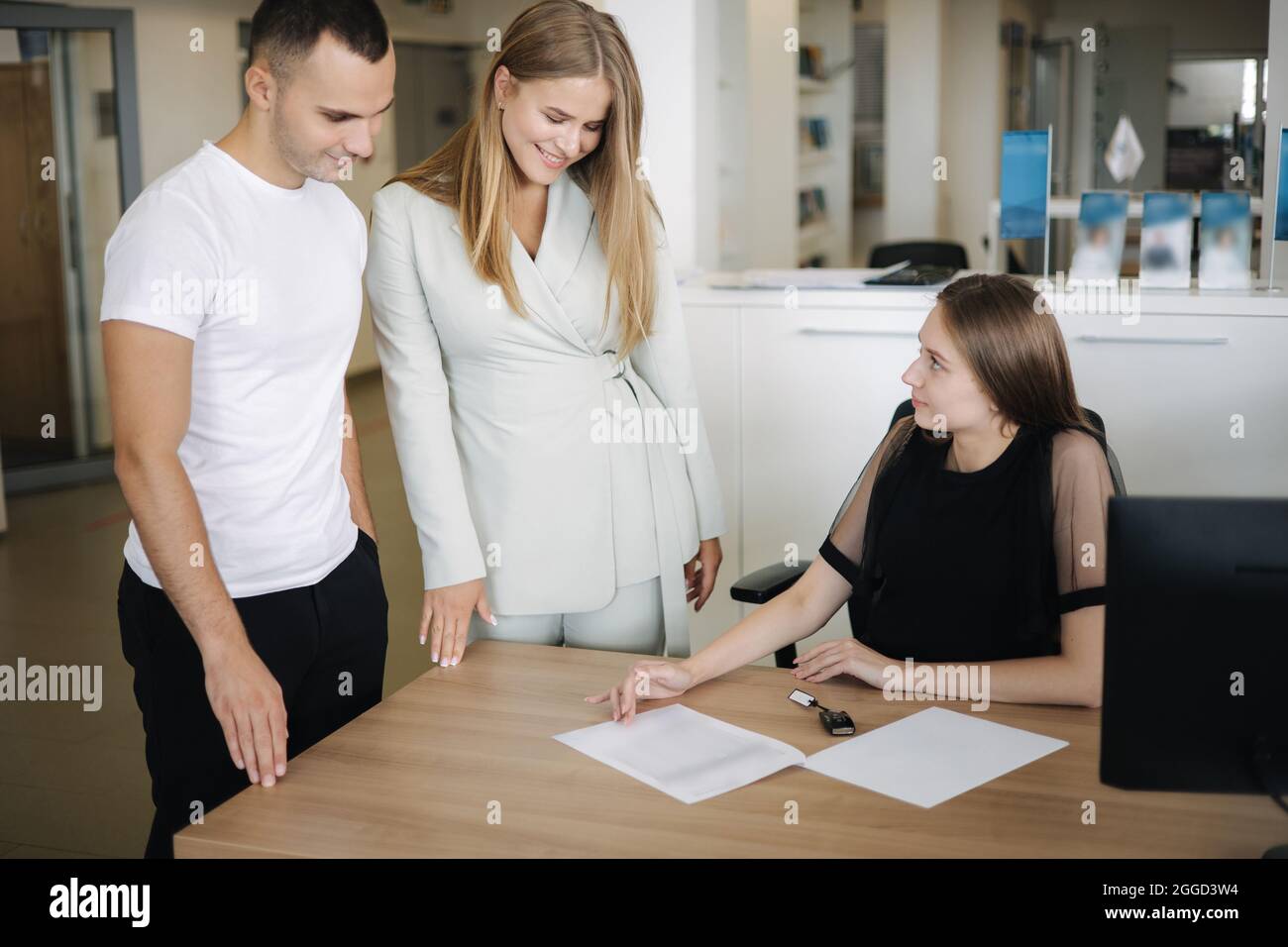 Giovane coppia che sceglie e acquista auto presso lo showroom auto. Il venditore di automobili li aiuta a prendere la giusta decisione Foto Stock