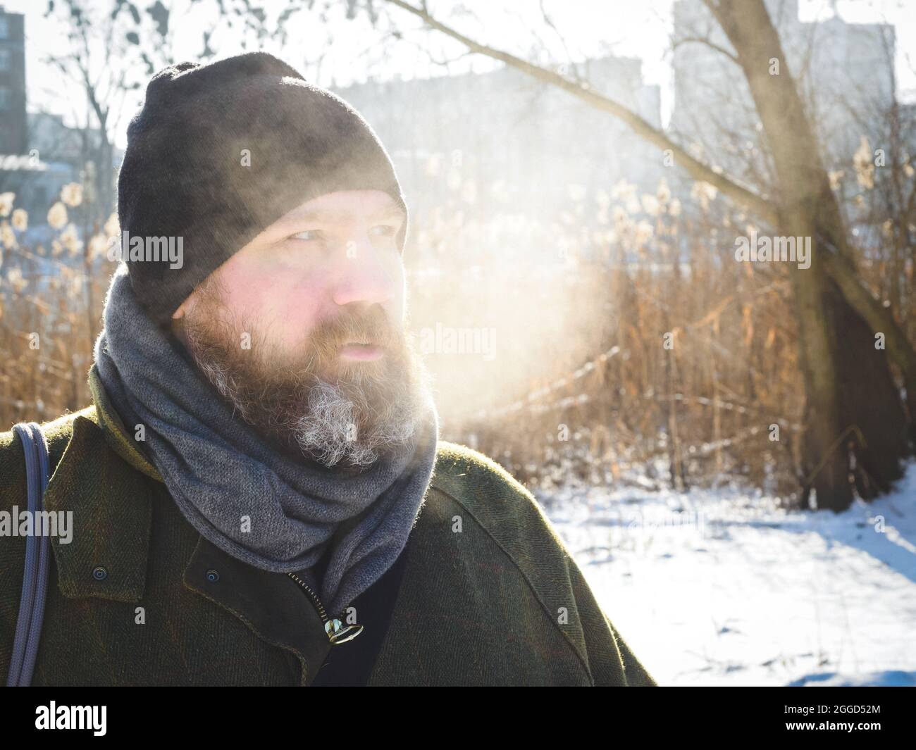 L'uomo respira aria fredda invernale in un parco. Uomo bearded che si distende sulla passeggiata di inverno nella foresta nevosa, cattura candid, scena di lifestyle Foto Stock