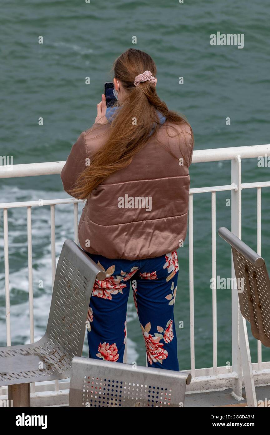 giovane donna che usa uno smartphone, giovane donna al mare che scatta una fotografia con un telefono, giovane donna che guarda il telefono sulla costa, giovane donna testo. Foto Stock