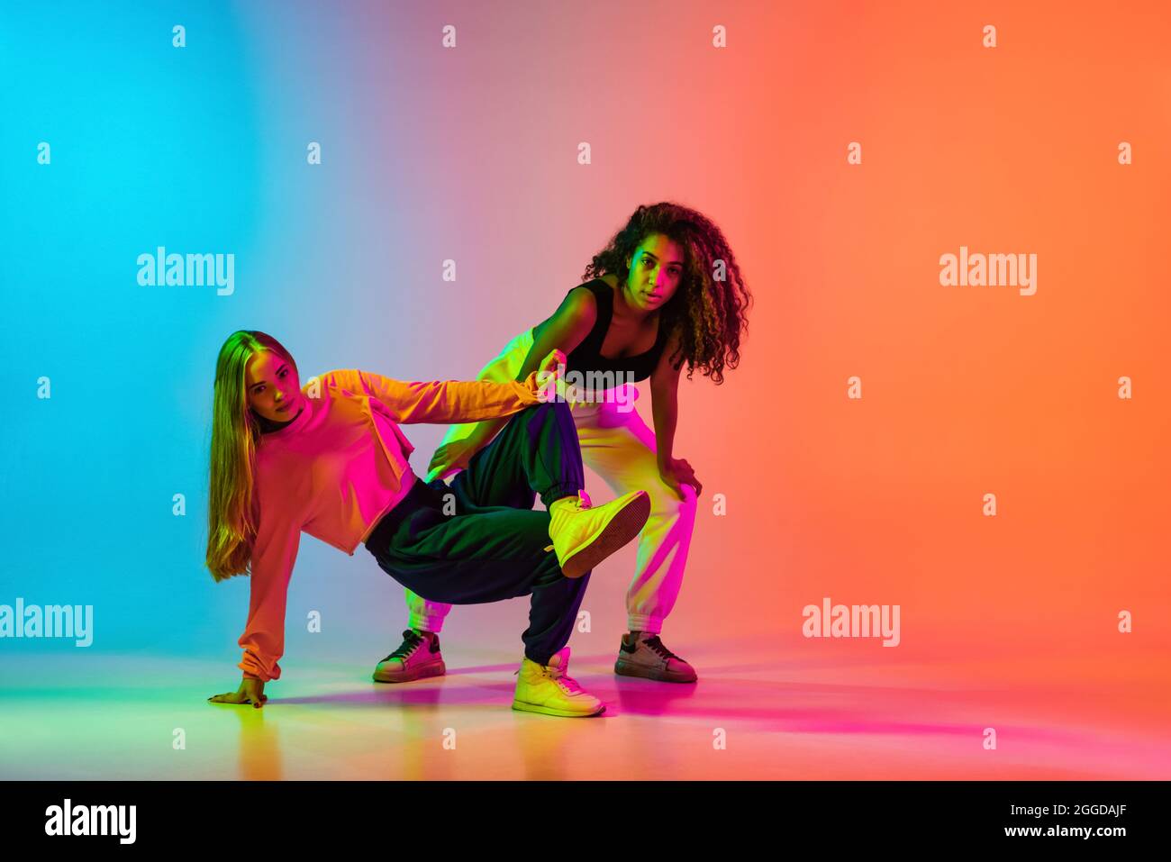 Rima. Due ragazze moderne ed eleganti che ballano hip-hop su sfondo blu  arancione sfumato in neon Foto stock - Alamy