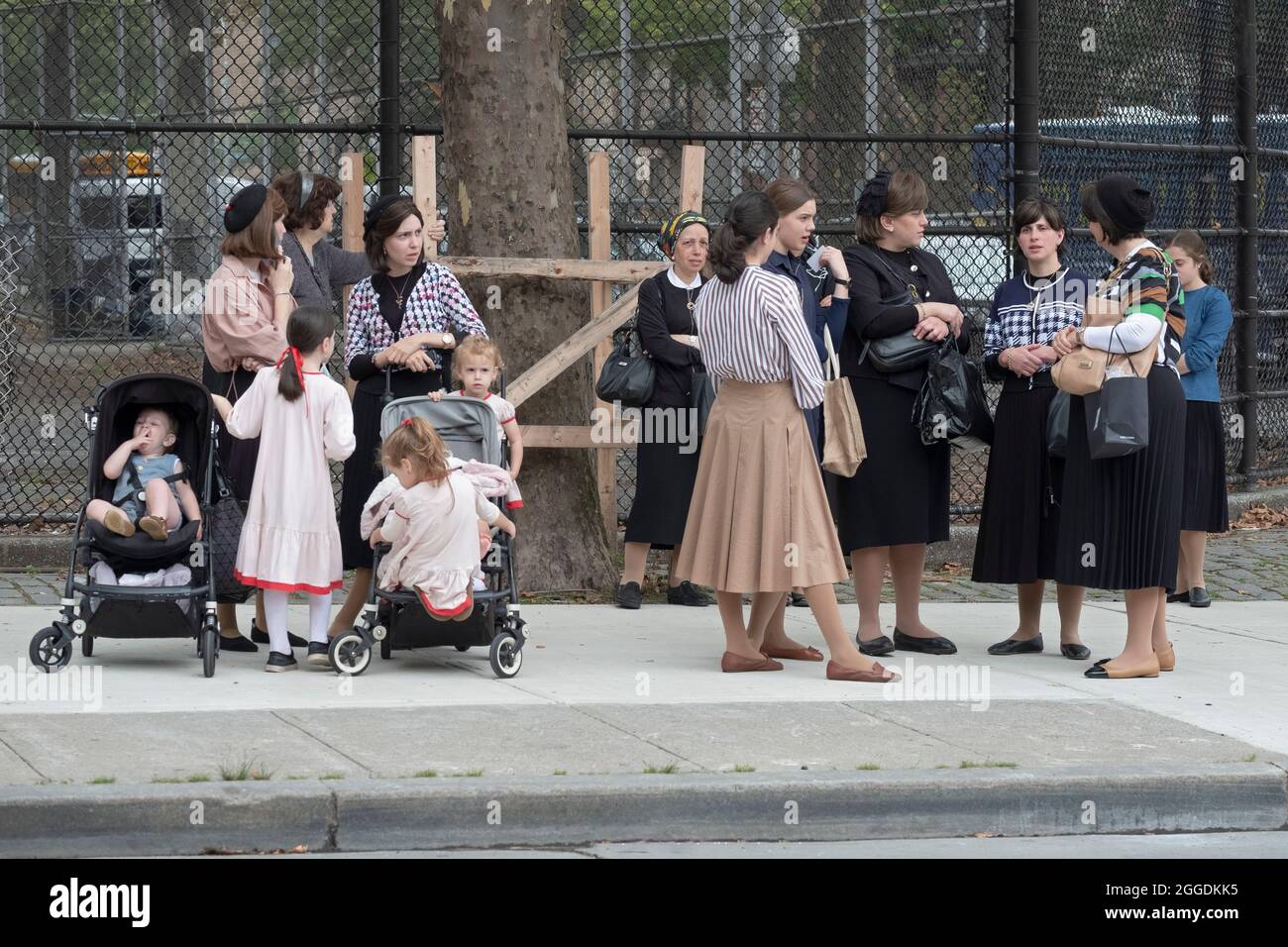 Un gruppo di madri e famiglie ebraiche ortodosse vestite modestamente aspetta un autobus scolastico per arrivare con i loro figli. A Williamsburg, Brooklyn, New York. Foto Stock
