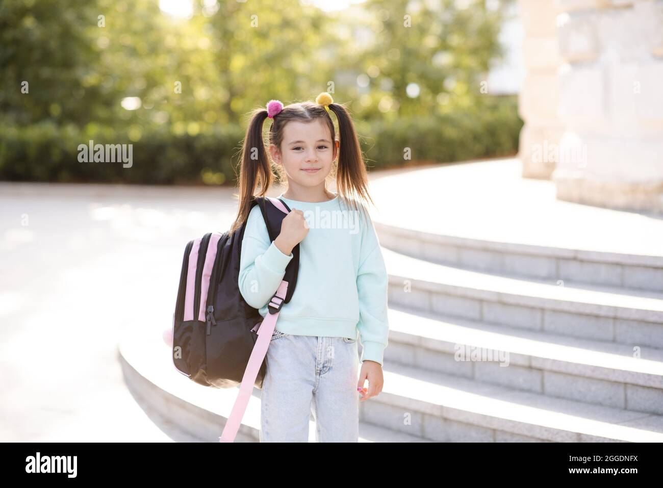 Sorridente dolce ragazza piccola felice 5-6 anni indossare abiti casual e zaino. Il bambino della pupilla si prepara per studiare. Torna a scuola. Stagione autunnale. Ha Foto Stock