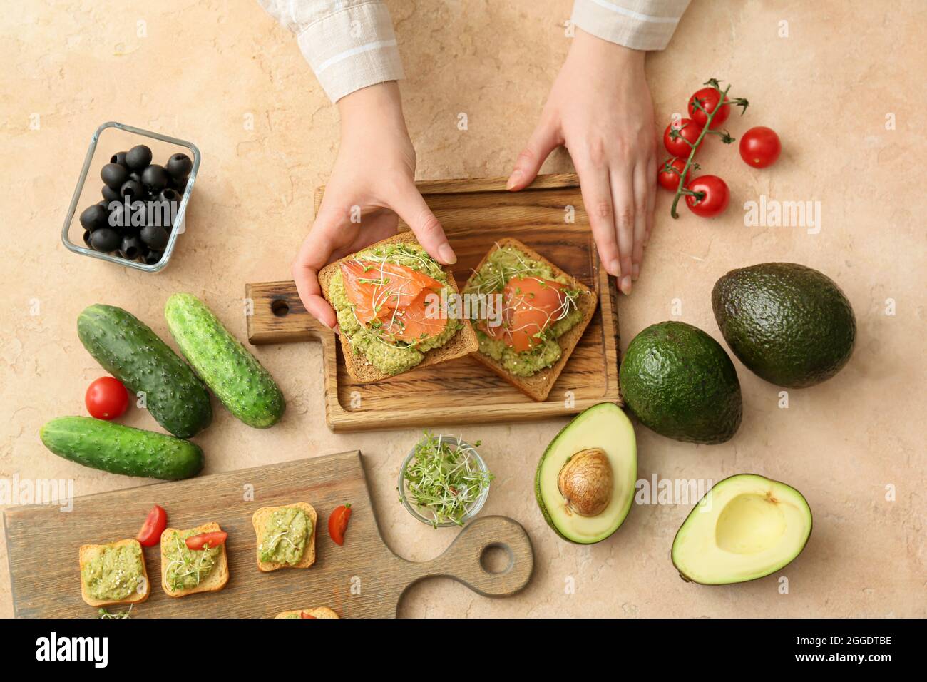 Donna che tiene gustosi sandwich con guacamole e salmone a tavola Foto Stock