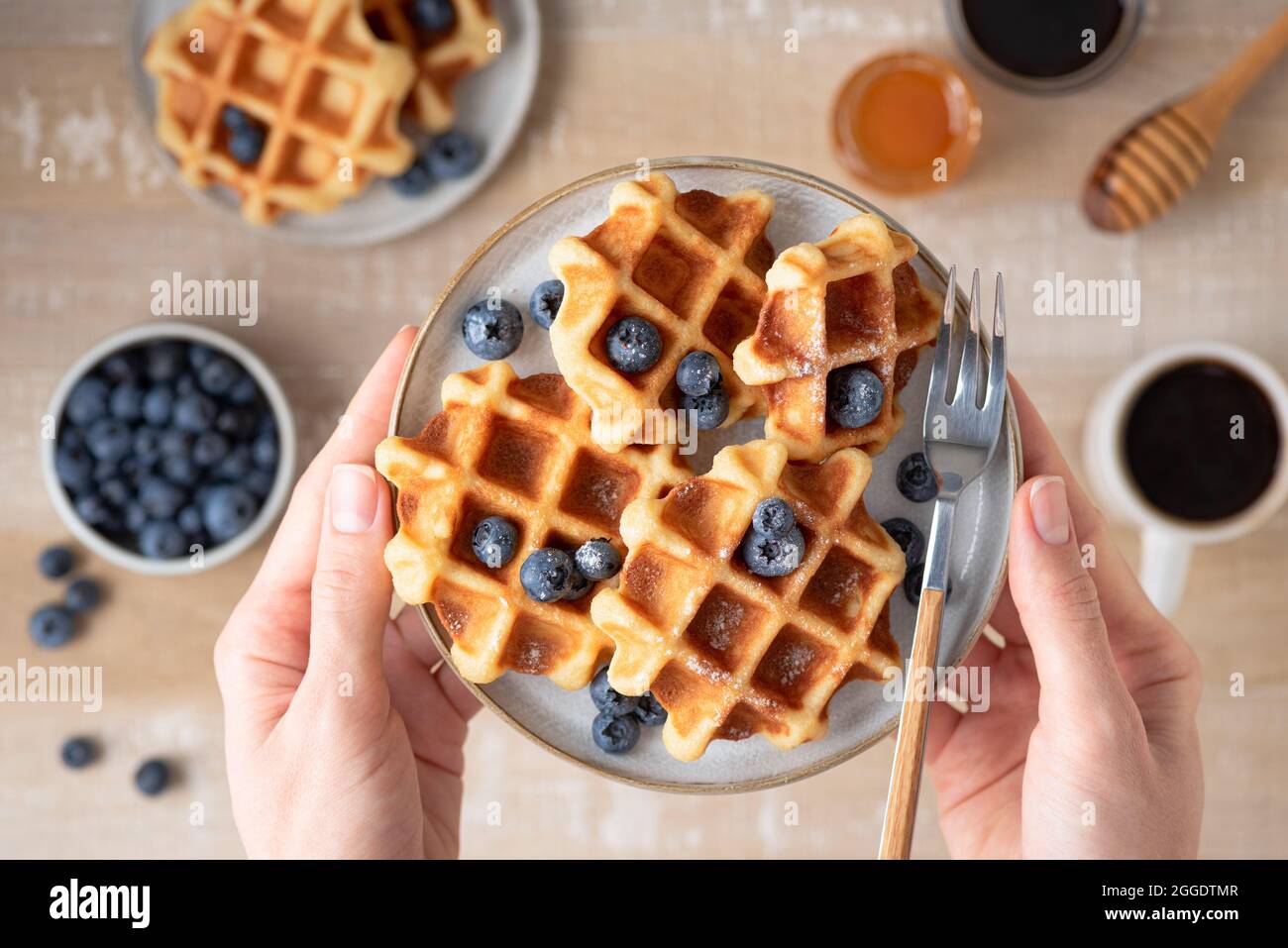 Waffle con mirtilli in mani femminili, tavolo per la colazione sullo sfondo. Vista dall'alto Foto Stock