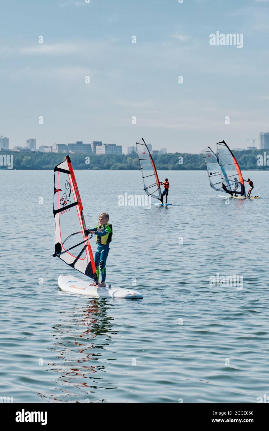 Corsi di windsurf. Diversi bambini galleggiano a bordo con vela sul lago Foto Stock