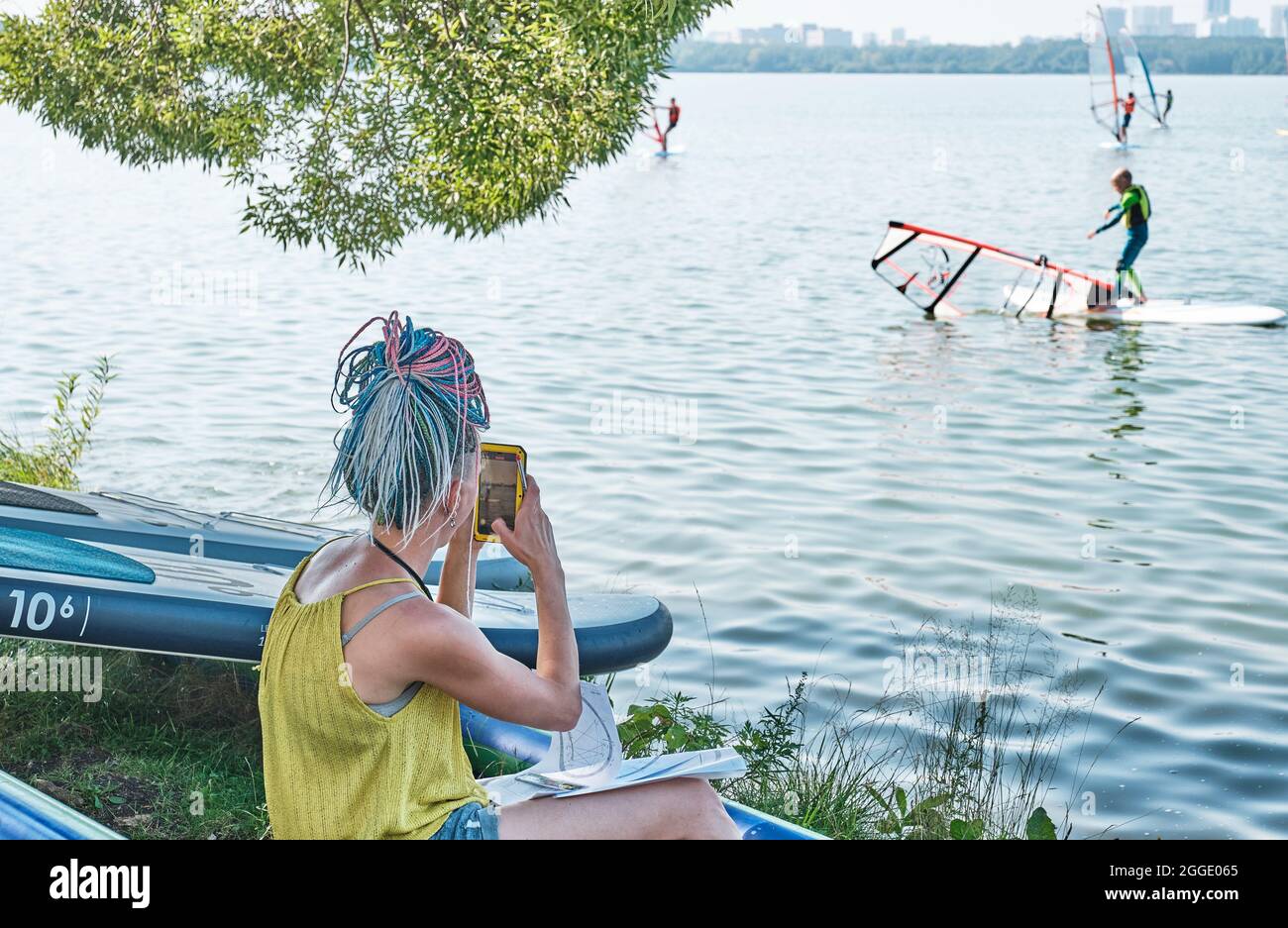 Ragazza con dreadlocks colorati scattare foto sul telefono di allenamento di windsurf Foto Stock