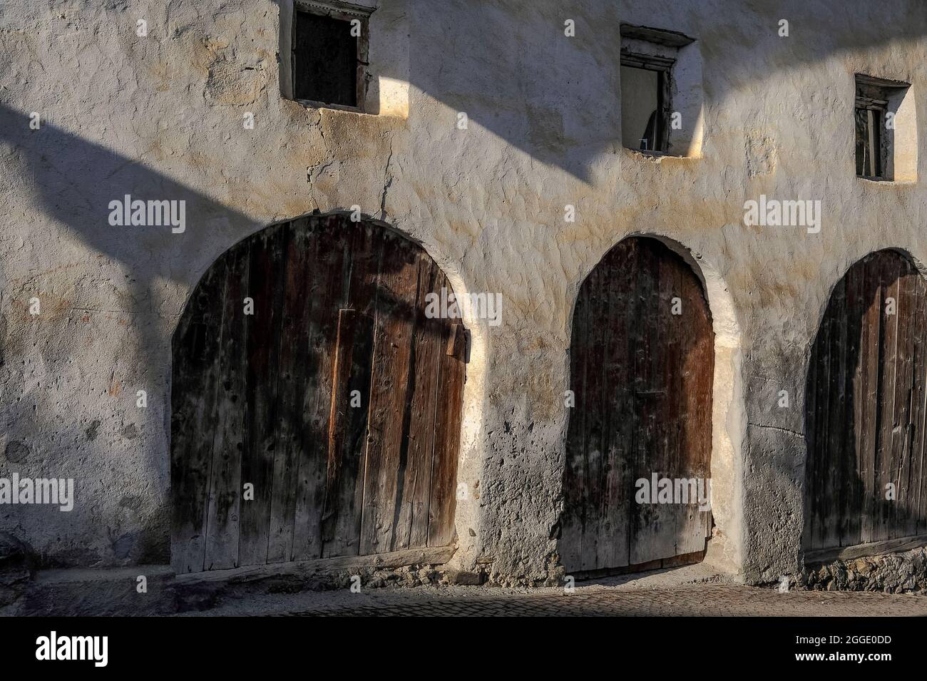 Le antiche porte non restaurate sono piene di porte a doghe rustiche sotto  una fila di piccole finestre profonde nel muro di pietra di una dimora  nella parte più antica della storica