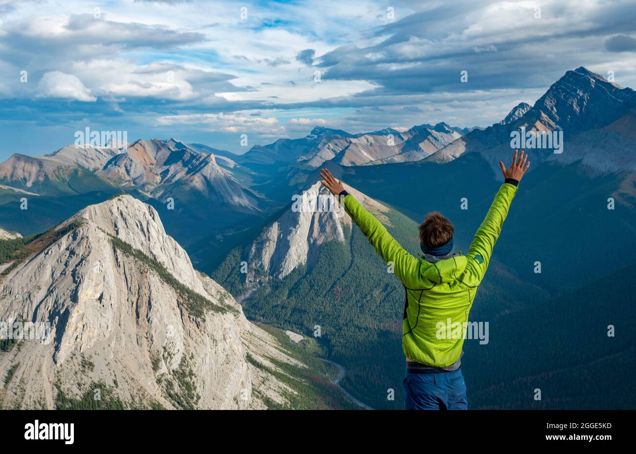 Escursionista stende le braccia nell'aria, paesaggio di montagna con valle del fiume e cime, cime con depositi di zolfo arancione, rovesciamento montagna, panoramica Foto Stock