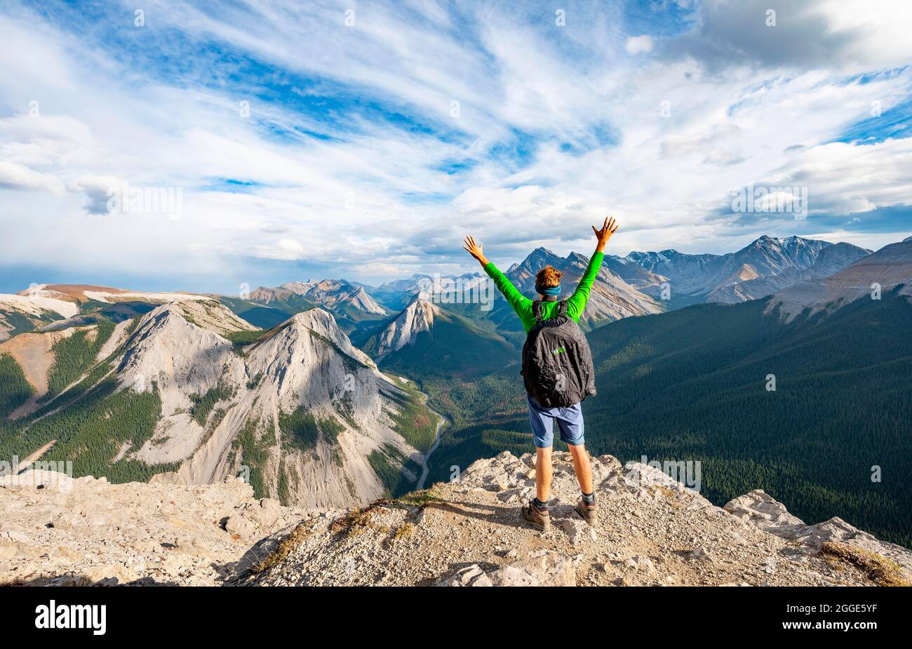 Escursionista allunga le braccia in aria, paesaggio di montagna con valle del fiume e cime, cime con giacimenti di zolfo arancio, rovesciamento montagna, panoramica Foto Stock