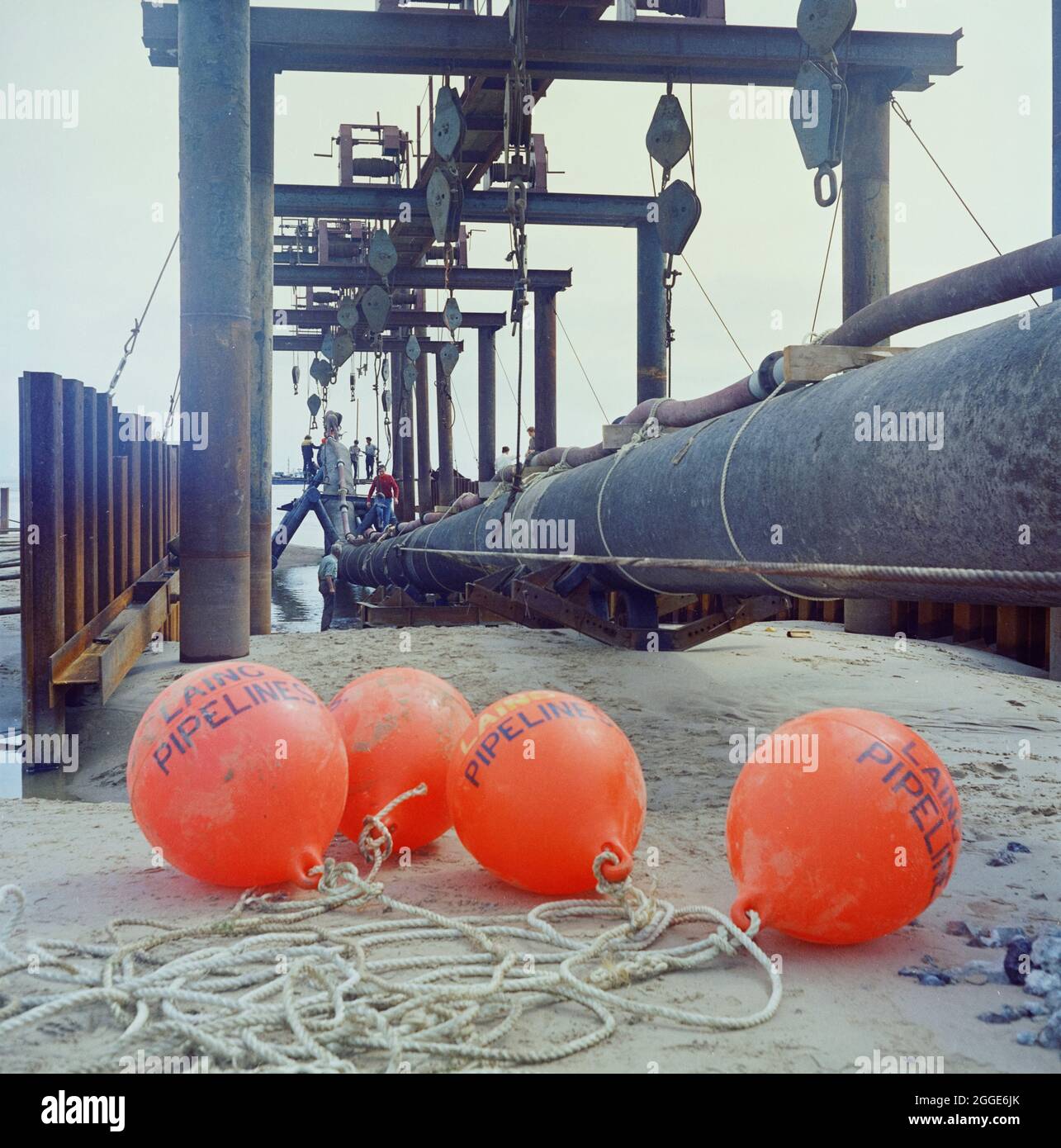 Una vista del sito di lancio del gasdotto North Coates, che mostra le boe dei gasdotti di Laing in primo piano con il gasdotto e le attrezzature di sollevamento in background. I lavori di ingegneria civile sul gasdotto North Coates sono stati eseguiti da Laing Pipelines insieme alle società francesi Entrepose e GTM, e il principale appaltatore per i lavori di dragaggio era Dreging and Construction Company insieme ad Adriaan Volker di Rotterdam. Oltre due miglia di 36 pollici di diametro pipeline, racchiusi in calcestruzzo, è stato tirato fuori in mare nell'estuario dell'Humber il 16 giugno 1970. Foto Stock
