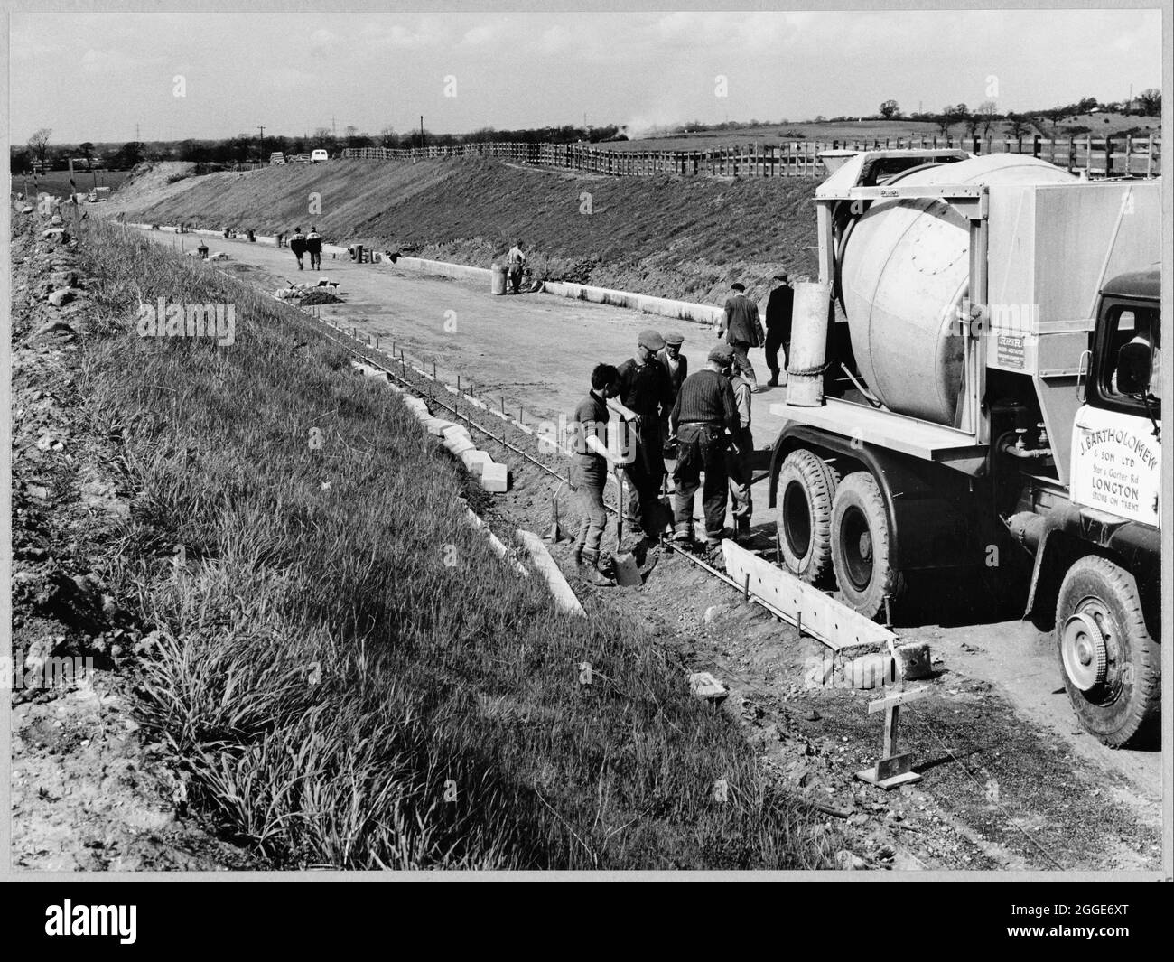 Una vista della costruzione della Birmingham a Preston autostrada (M6), guardando a nord lungo una strada di scorrimento sul lato est della sezione D dell'autostrada e mostrando un gruppo di uomini in primo piano, in piedi accanto ad un camion betoniera. I lavori sull'autostrada da Birmingham a Preston (M6), tra gli svincoli da J13 a J16 iniziarono nel giugno 1960 e furono eseguiti da John Laing Construction Ltd. La sezione D era di 7 1/2 miglia di lunghezza tra Keele e Barthomley. Foto Stock