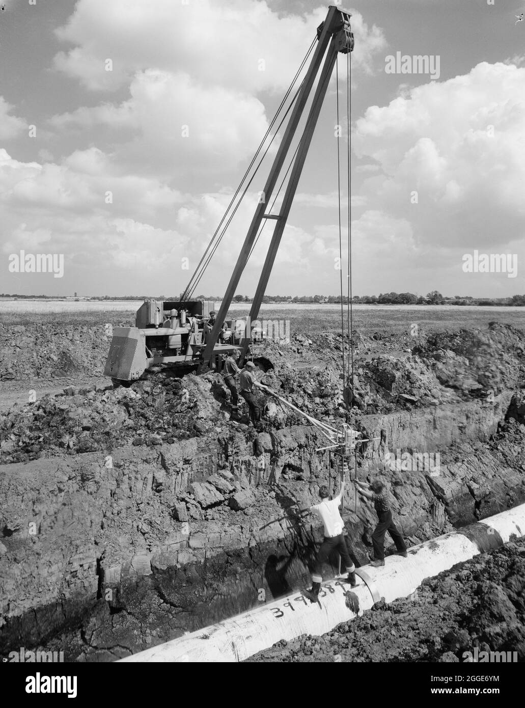 Un gasdotto con un braccio laterale e un team di lavoratori che posano una sezione del gasdotto Fens in una trincea. I lavori per la posa del gasdotto Fens sono iniziati nel giugno 1967 e sono stati una joint venture tra Laing Civil Engineering e le società francesi Entrepose e Grands Travaux de Marseille (GTM) per il Consiglio del gas. Oltre 600 uomini hanno lavorato al progetto per posare tubi in acciaio di diametro 36 pollici a partire da West Winch a Norfolk e fino a dove si è collegato con il prossimo contratto a Woodcroft Castle a Cambridgeshire. Il gasdotto attraversava quattro fiumi e numerose dighe e fossati. Foto Stock
