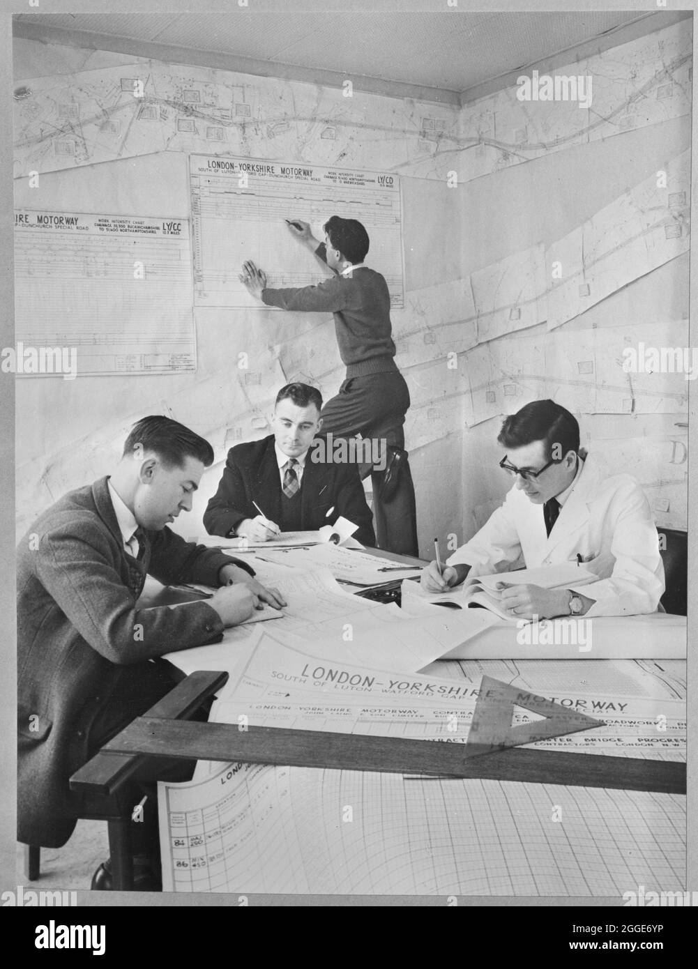 Quattro impiegati, probabilmente presso la sede del progetto a Newport Pagnell, aggiornano le carte e tracciano i progressi nella costruzione della London to Yorkshire Motorway (M1). Questa immagine è stata catalogata come parte del Breaking New Ground Project in collaborazione con il John Laing Charitable Trust nel 2019-20. Foto Stock