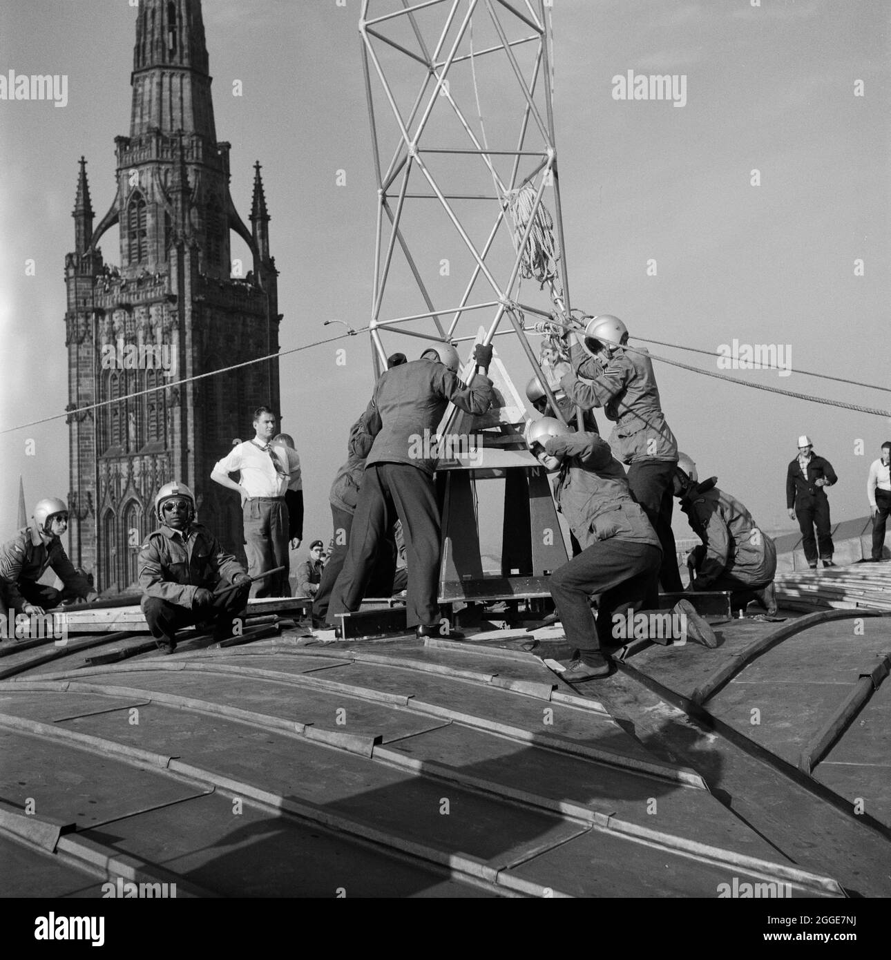 L'equipaggio di RAF sul tetto della Cattedrale di Coventry manovrando la guglia di bronzo da 80 piedi su una piastra quadrata da 1 iarda. La guglia della vecchia cattedrale è visibile sullo sfondo. La fotografia è stata scattata durante l'operazione Rich Man, un progetto congiunto che coinvolse il personale dell'Aeronautica reale e il personale di Laing. Questo ha coinvolto un elicottero belvedere RAF che si è issato per posizionare la guglia di bronzo da 80 piedi sulla nuova cattedrale. La parte dell'operazione di abbassamento della traversa di 1/2 tonnellate che si trova sulla sommità della guglia doveva essere posticipata a causa delle condizioni di vento. Foto Stock