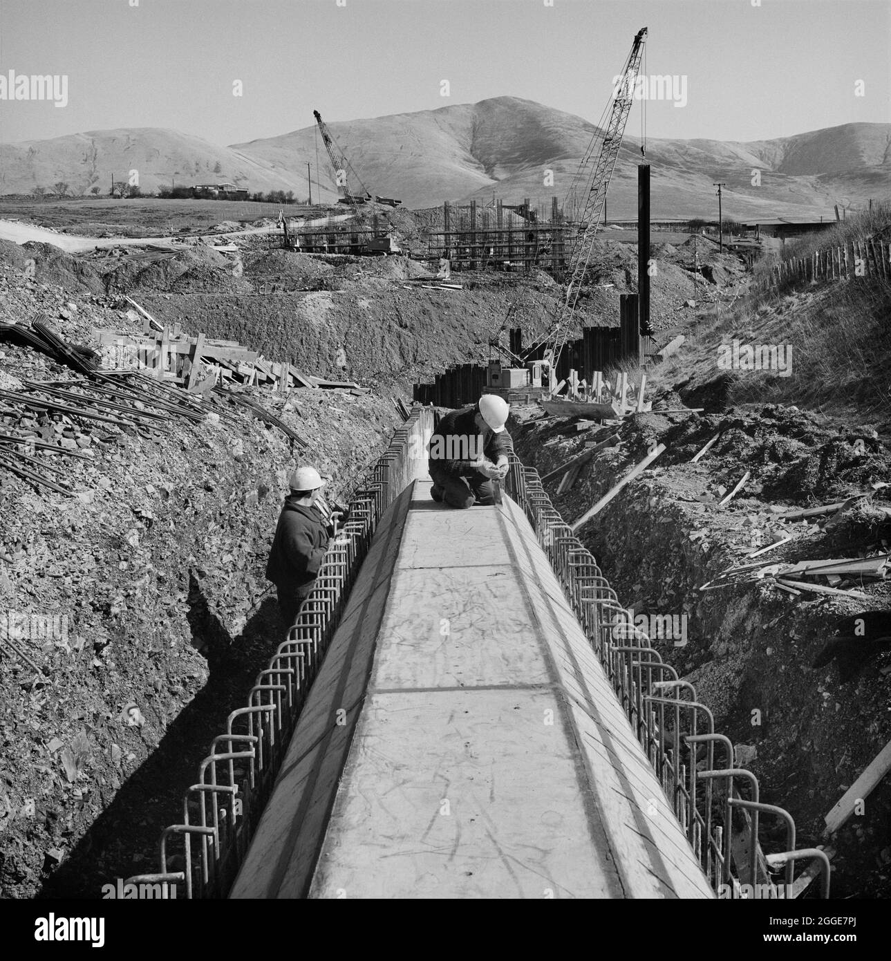 Un team di due persone che lavorano su un box culvert durante la costruzione dell'autostrada M6 attraverso la Gola di Lune. I lavori sulla sezione Lune Gorge dell'autostrada M6 tra Killington e Tebay (Junction 37 - Junction 38) sono stati eseguiti da John Laing Construction Ltd. I lavori sono iniziati nell'ottobre 1967 e l'autostrada è stata aperta al traffico nell'ottobre 1970. Per il progetto, Laing aveva la sede centrale a Lowgill. Questa fotografia è stata pubblicata nel maggio 1968 nella newsletter mensile 'Team Spirit' ed è intitolata 'Wishbone box culvert'. Foto Stock