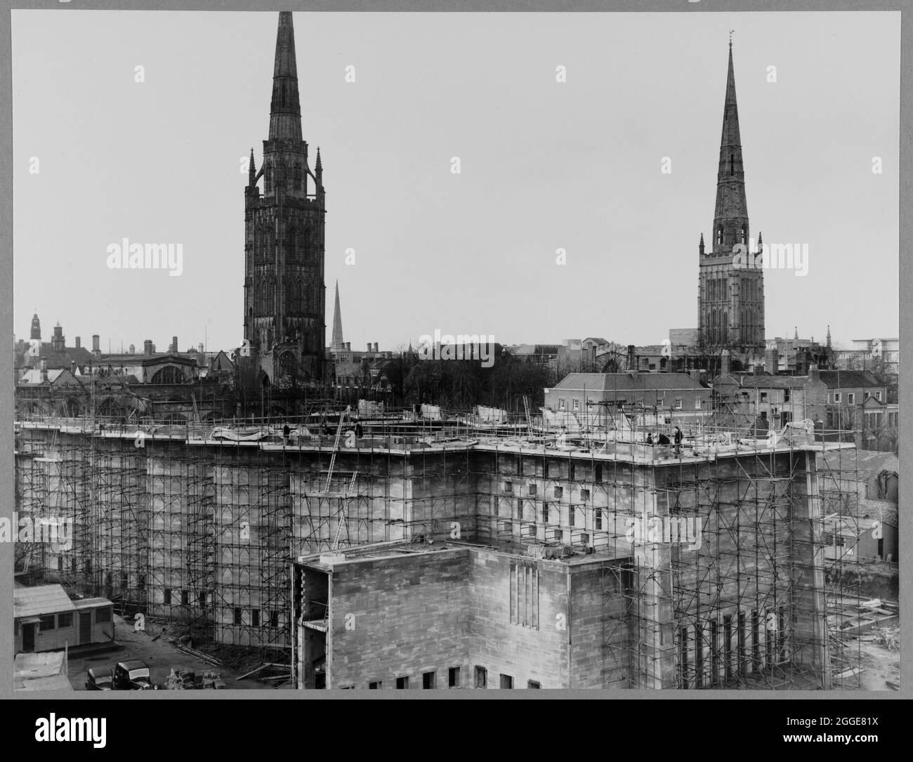 Una vista da nord-est che mostra le mura nord ed est della Cattedrale di Coventry durante la sua costruzione, con la vecchia cattedrale e la Chiesa della Santissima Trinità sullo sfondo. Dopo il bombardamento della Cattedrale di Coventry nel novembre 1940, nel 1950 è stato lanciato un concorso per trovare un progetto per una nuova cattedrale. Il progetto vincente è stato di Sir Basil Spence (1907-1976) da uno degli oltre 200 disegni presentati. Tra la metà degli anni '50 e il 1962 si svolsero lavori di costruzione. La regina Elisabetta II pose la pietra di fondazione il 23 marzo 1956. Foto Stock