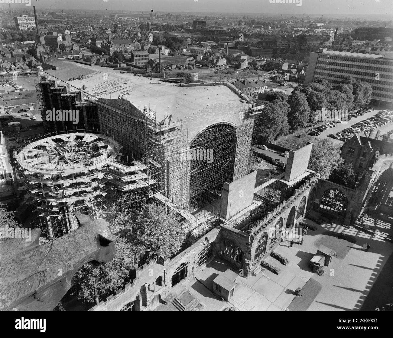 Una vista dalla guglia della Chiesa Cattedrale di San Michele, guardando in direzione nord-est sul sito di costruzione della nuova Cattedrale di Coventry, con le rovine della vecchia cattedrale in primo piano e la città di Coventry oltre. La fotografia mostra la costruzione della nuova Cattedrale di Coventry, progettata da Basil Spence nel 1951 e costruita tra la metà degli anni '50 e il 1962. Ha sostituito la rovinata Chiesa Cattedrale di San Michele, che era stata gravemente danneggiata dai bombardamenti del 1941. La fotografia è stata scattata per mostrare i progressi nella costruzione della cattedrale, incluso il roro in cemento Foto Stock