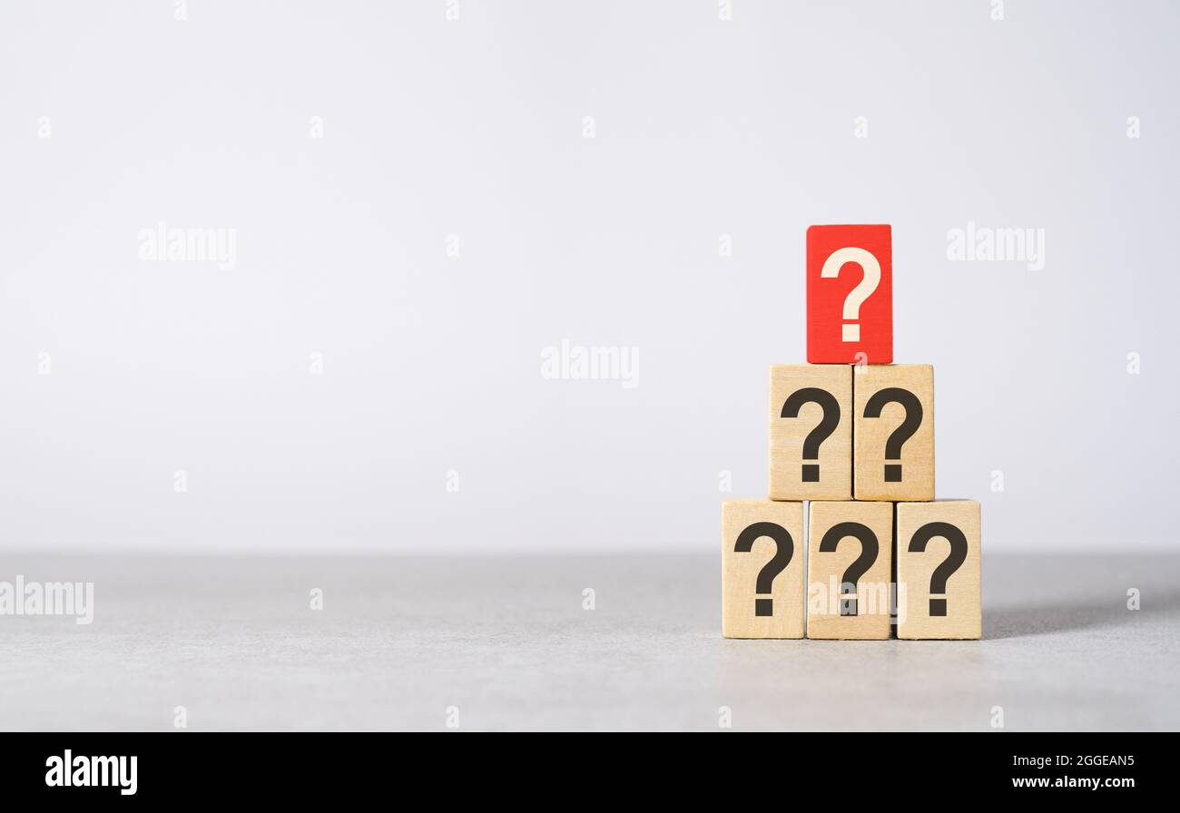 Concetto della domanda principale con un punto interrogativo stampato su un blocco di legno rosso sopra le altre domande nere con spazio per la copia su sfondo grigio chiaro. Foto Stock