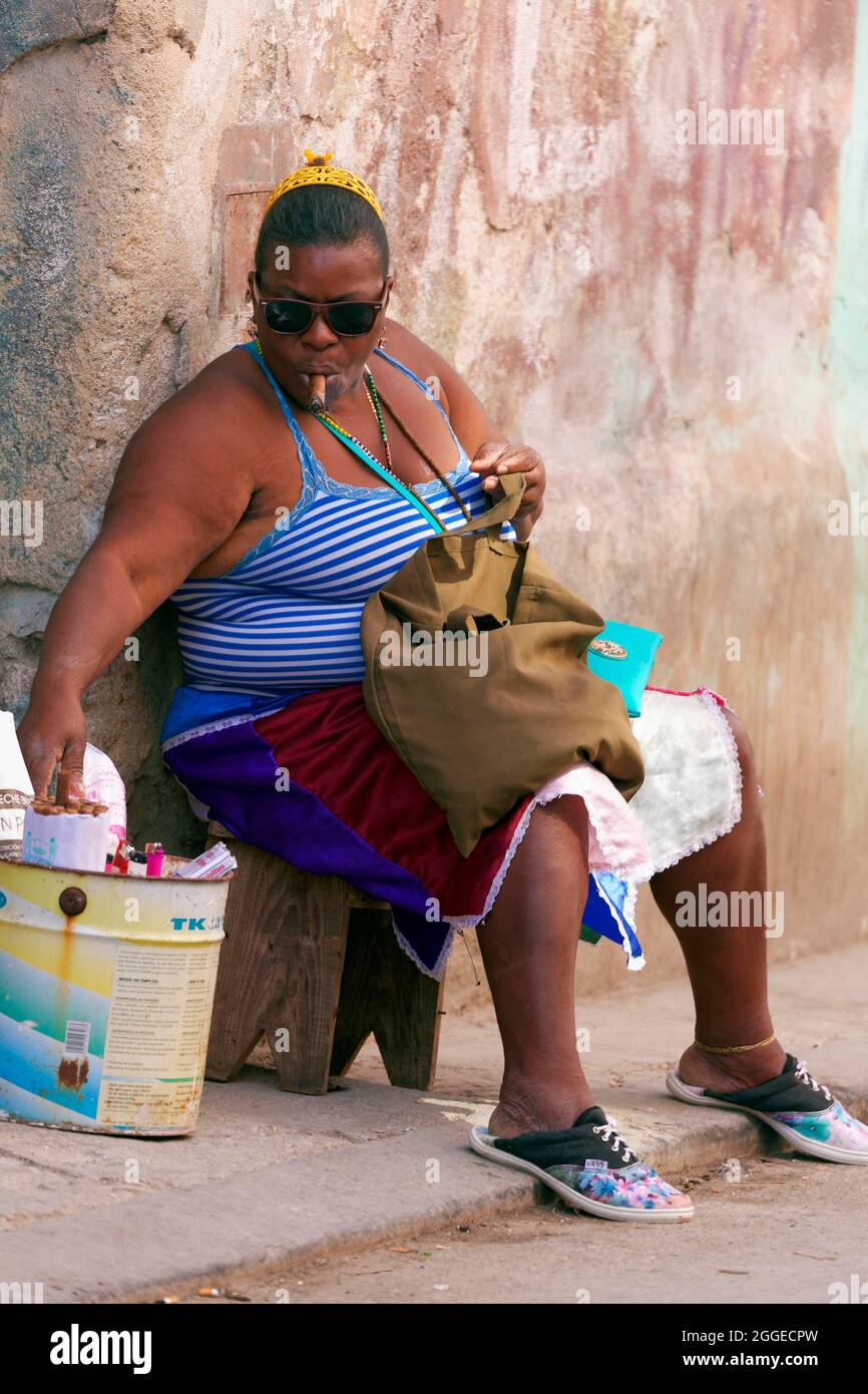 Donna cubana grassa, con pelle scura, cubana, seduta sullo sgabello davanti alla porta d'ingresso e sigaro fumante, Città Vecchia, capitale Avana, Provincia dell'Avana, Grande Foto Stock