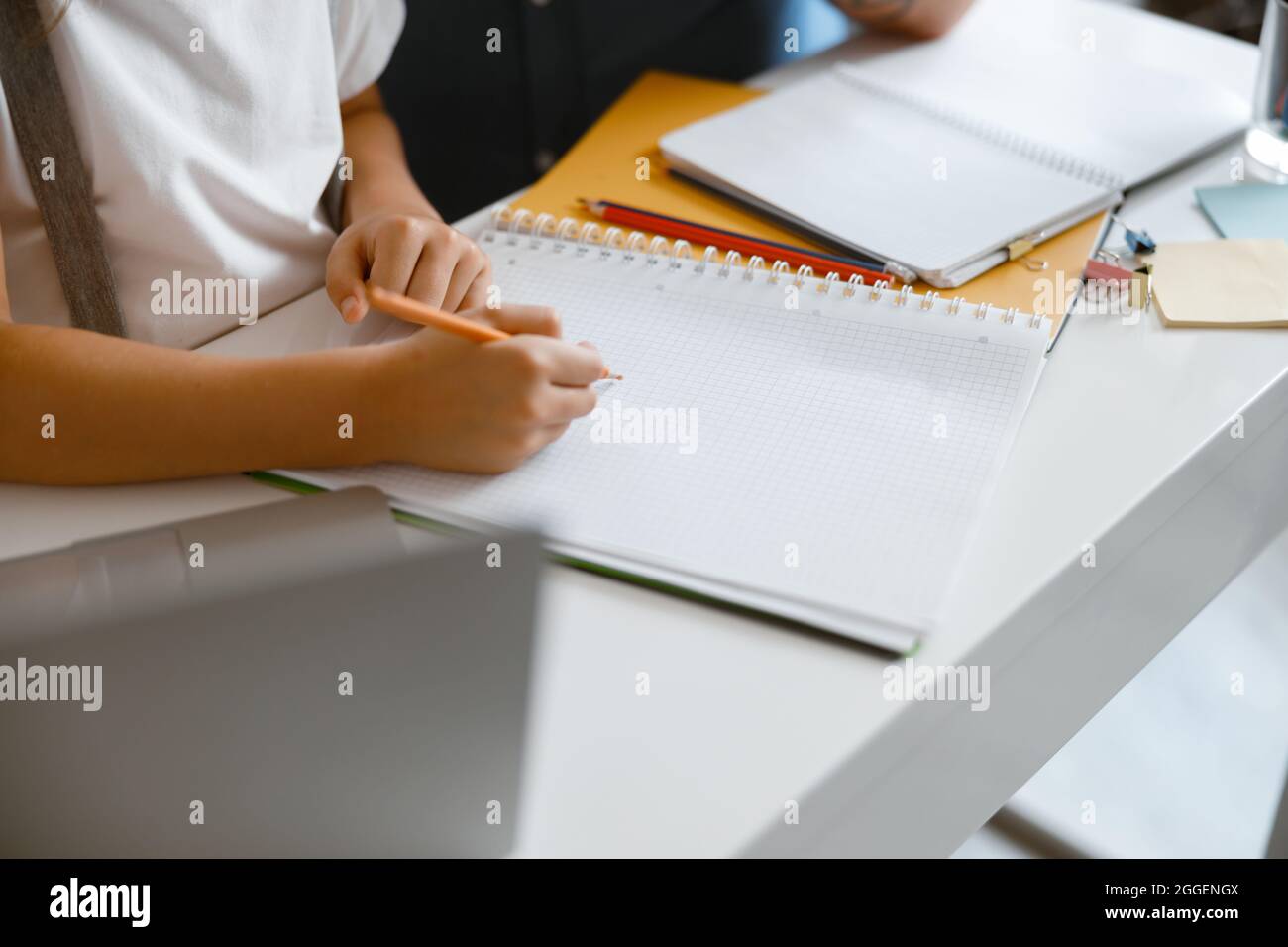 La ragazza piccola disegna in copybook con la matita gialla che fa i compiti al tavolo nella stanza Foto Stock
