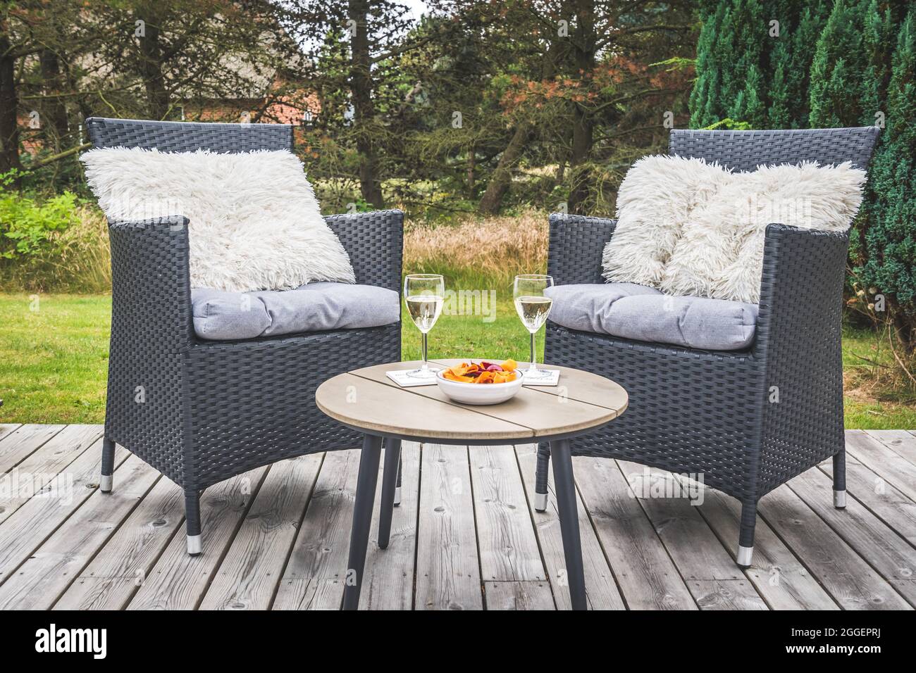 Due sedie in rattan con cuscini e un tavolino con bicchieri da vino su una terrazza in legno Foto Stock