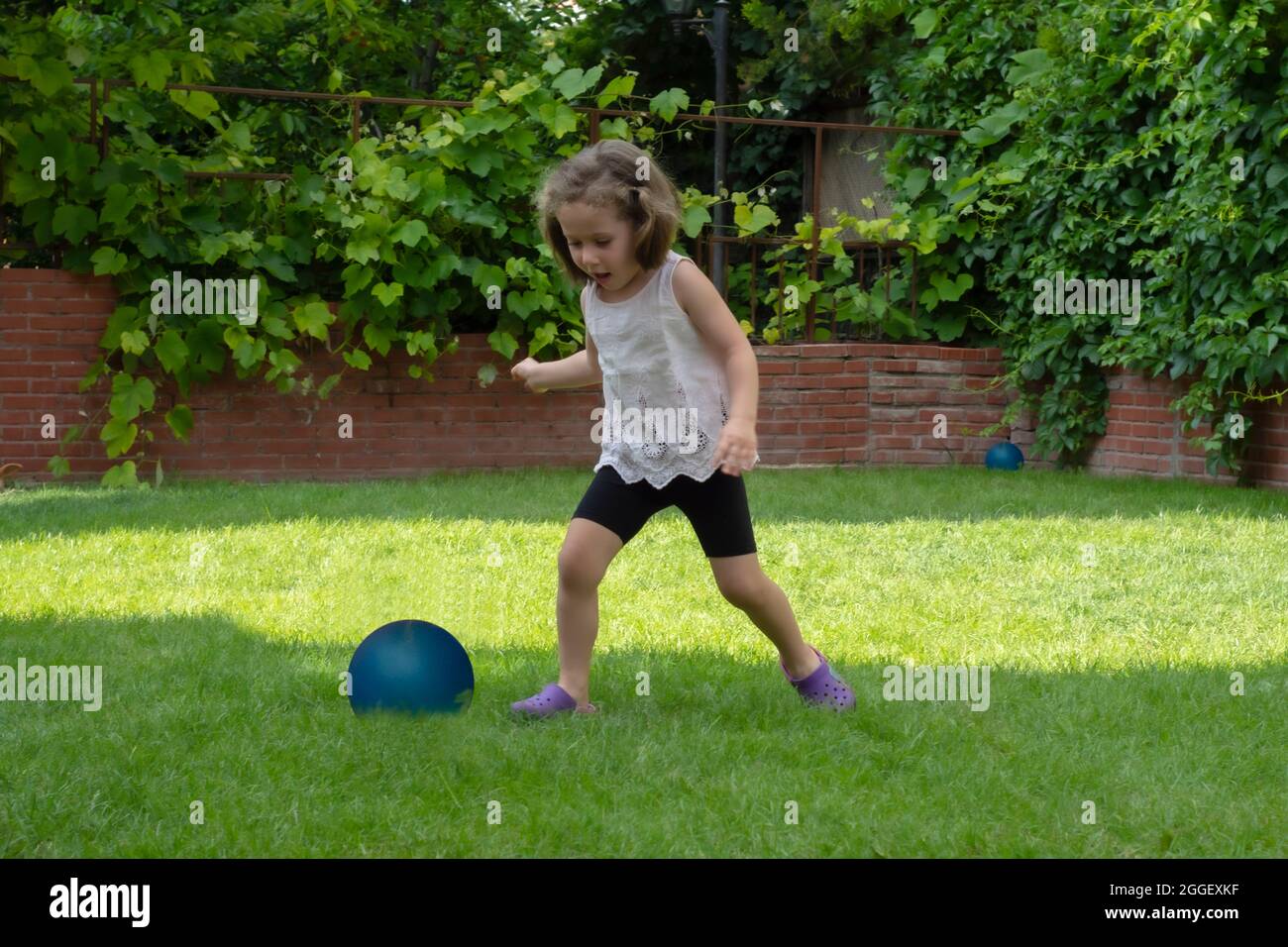 La bambina sta giocando con la sua palla blu nel giardino della loro casa. Focus Girl selettivo Foto Stock