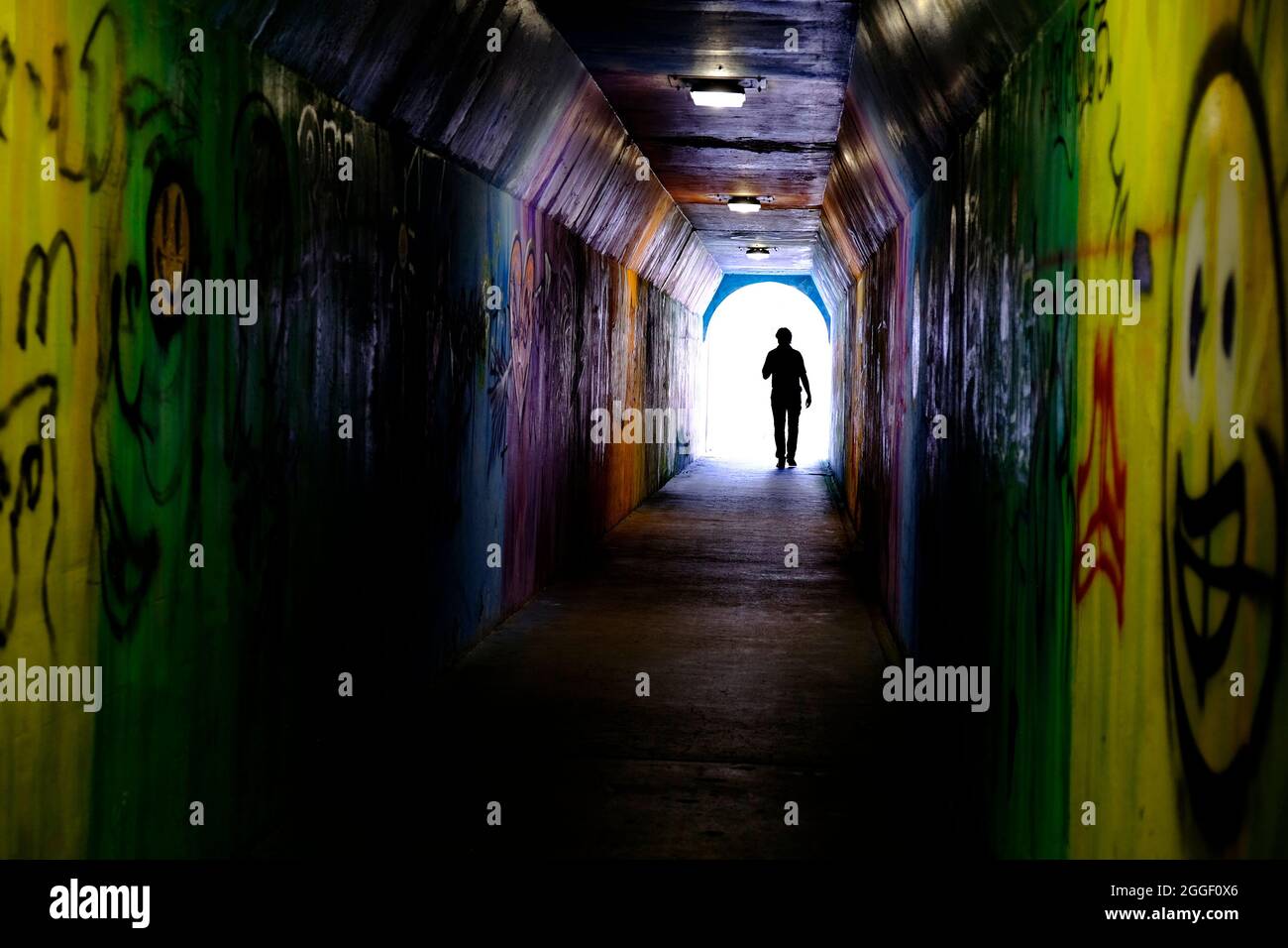 Uomo che cammina attraverso il tunnel dei graffiti verso la luce Foto Stock