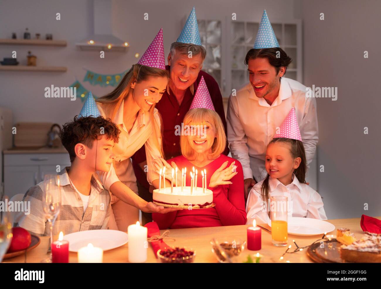 Famiglia allegra di multi generazione che ha festa di compleanno in serata, presentando torta donna anziana con candele, godendo la vacanza, avendo grande tempo di Toge Foto Stock