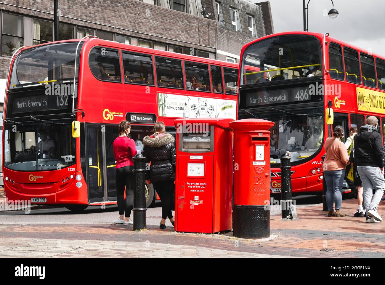 Bexleyheath Kent Inghilterra 08.31.21 due autobus rossi passano su una strada. Scatole per la raccolta di lettere e pacchi Royal Mail. Persone in attesa di imbarco pubblico Foto Stock