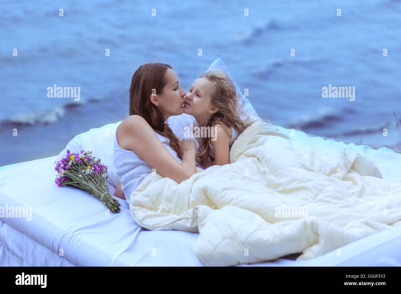 La donna e la figlia si trovano su un letto vicino all'oceano. Le onde si splaschano sullo sfondo. Foto Stock