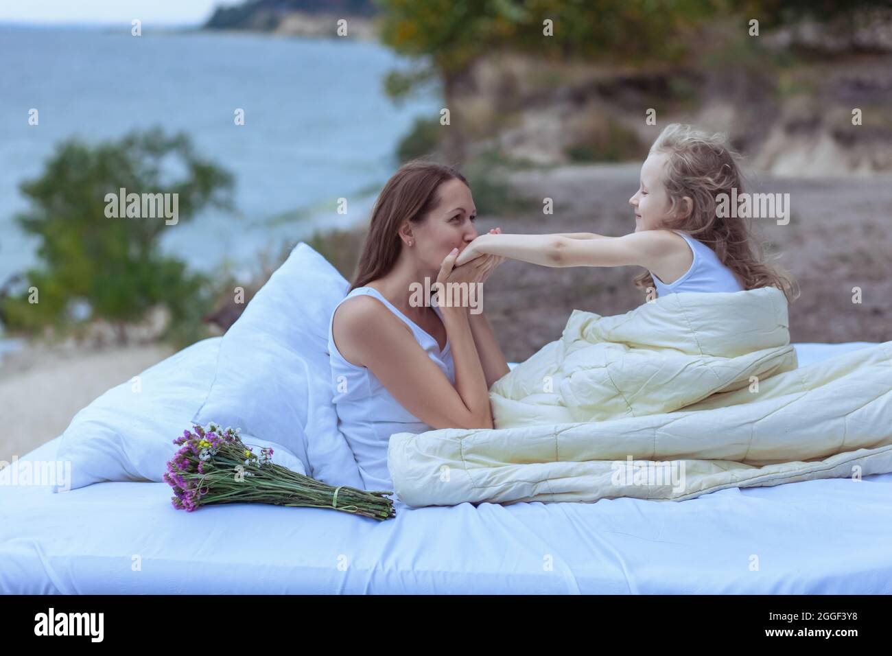 La donna bacia le mani della figlia. Zhenzhina e un bambino in un letto vicino all'oceano. Foto Stock