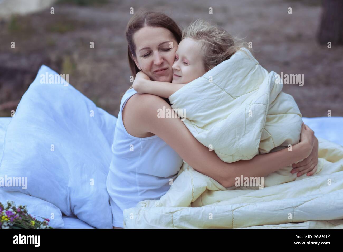 La donna abbraccia il bambino mentre si siede sul letto. Il bambino è coperto da una coperta all'aperto. Foto Stock