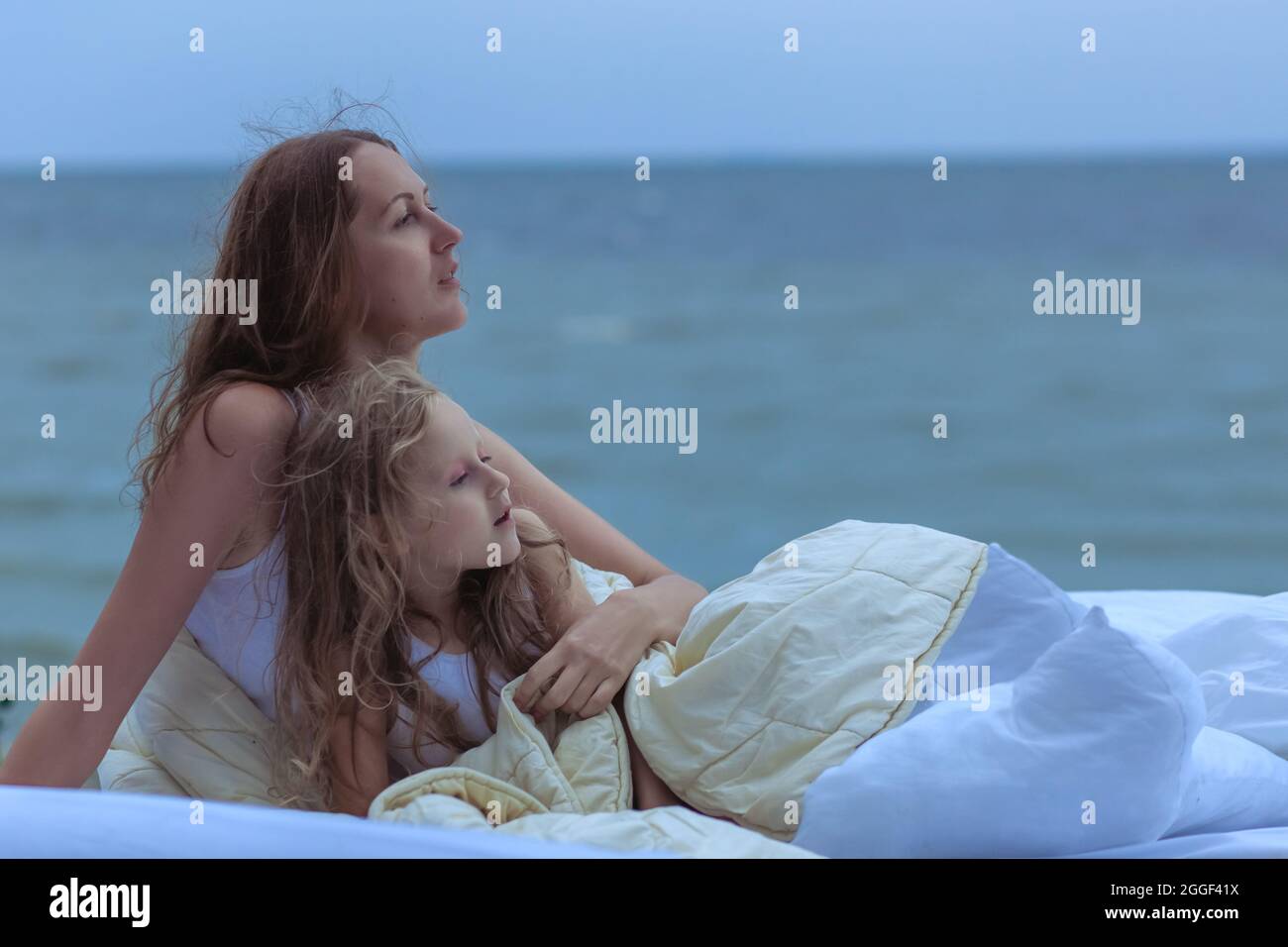 Donna e bambino guardano l'oceano mentre si siedono a letto. Si svegliarono sulla riva dell'oceano e sognarono di godere di un bellissimo paesaggio. Foto Stock