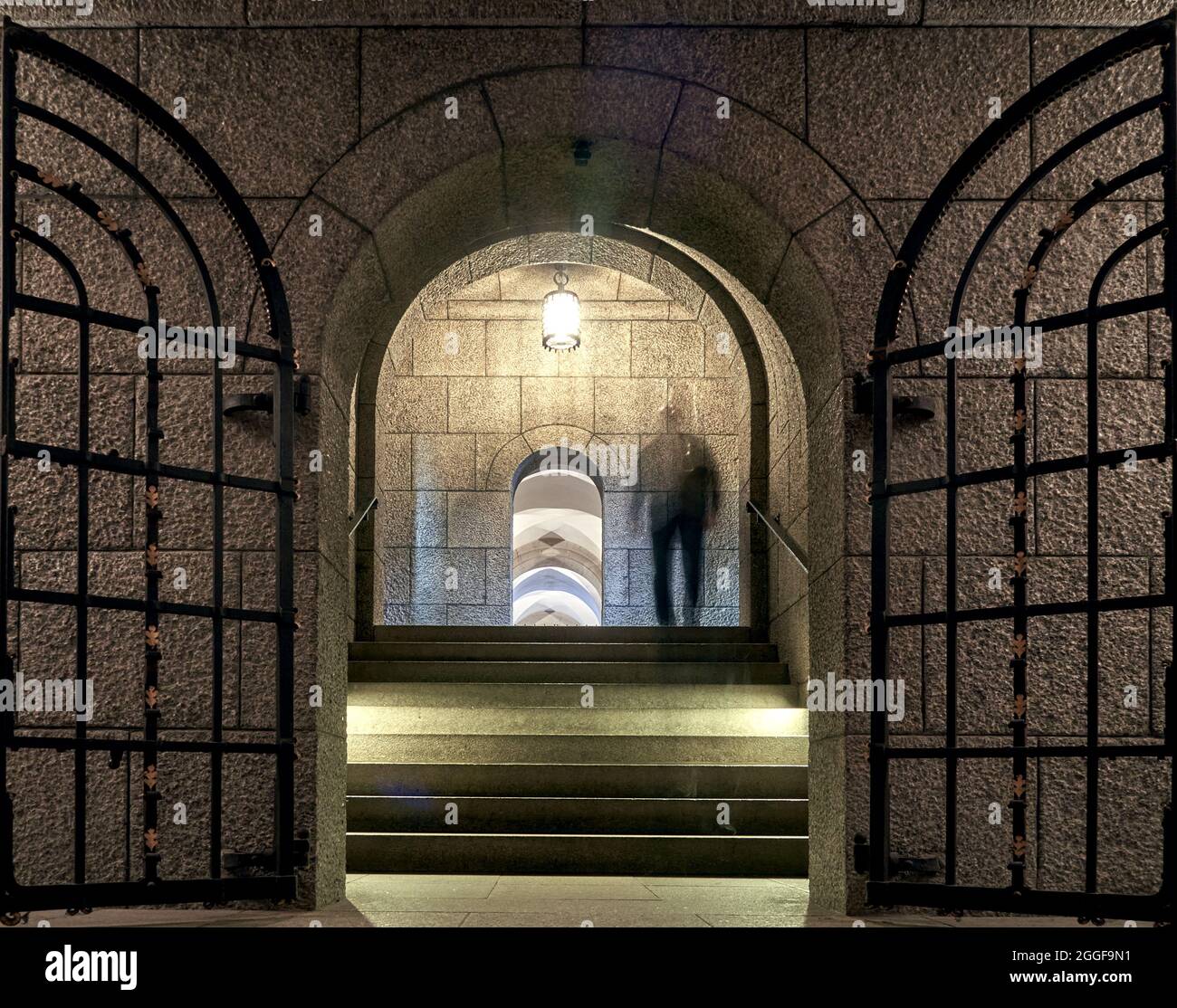 Scala con un cancello di ferro in una cripta di una cattedrale cristiana, fantasma umano sui gradini a causa di movimento sfocato Foto Stock