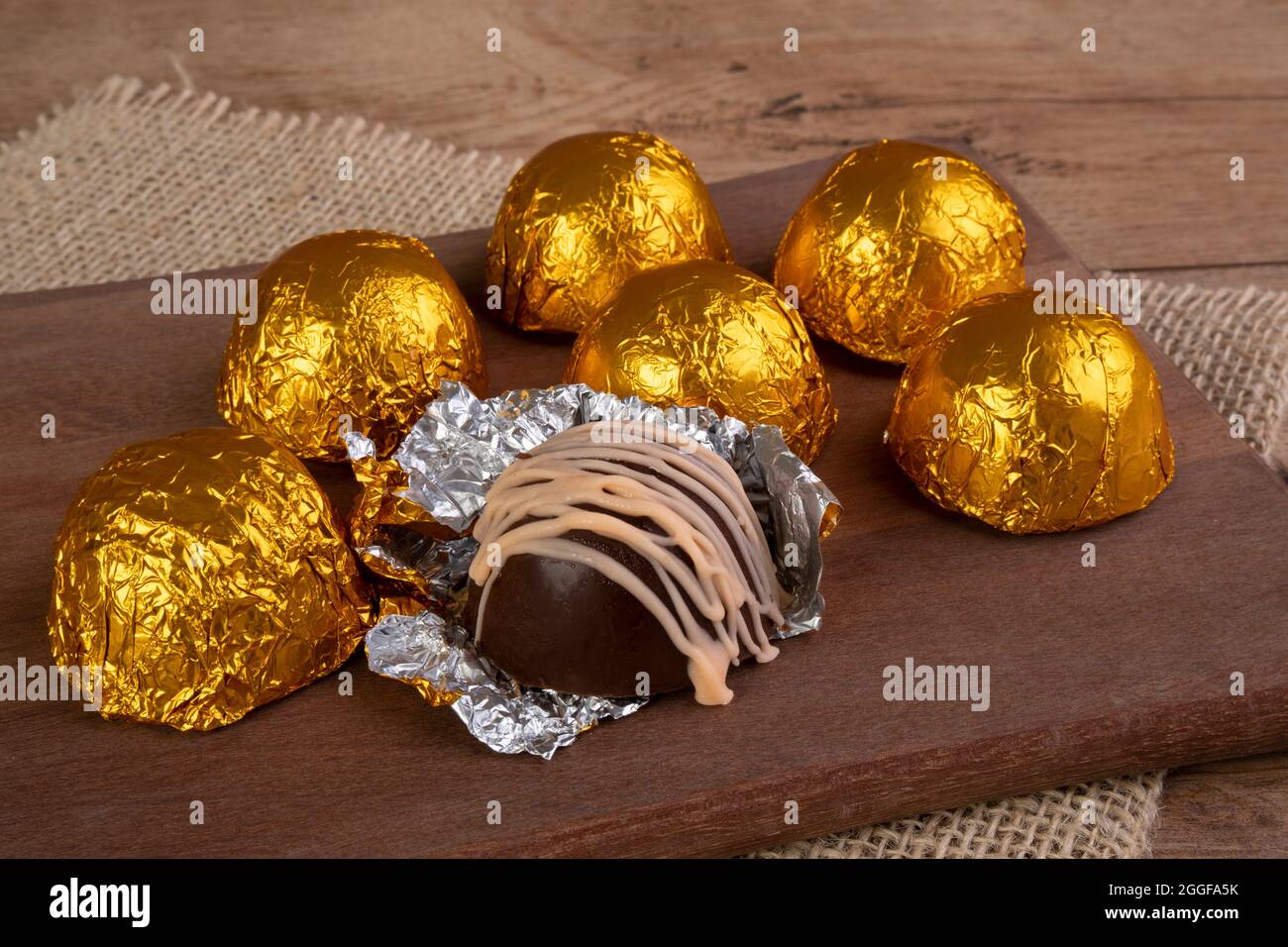 tartufi di cioccolato avvolti in carta laminata su tagliere di legno Foto Stock