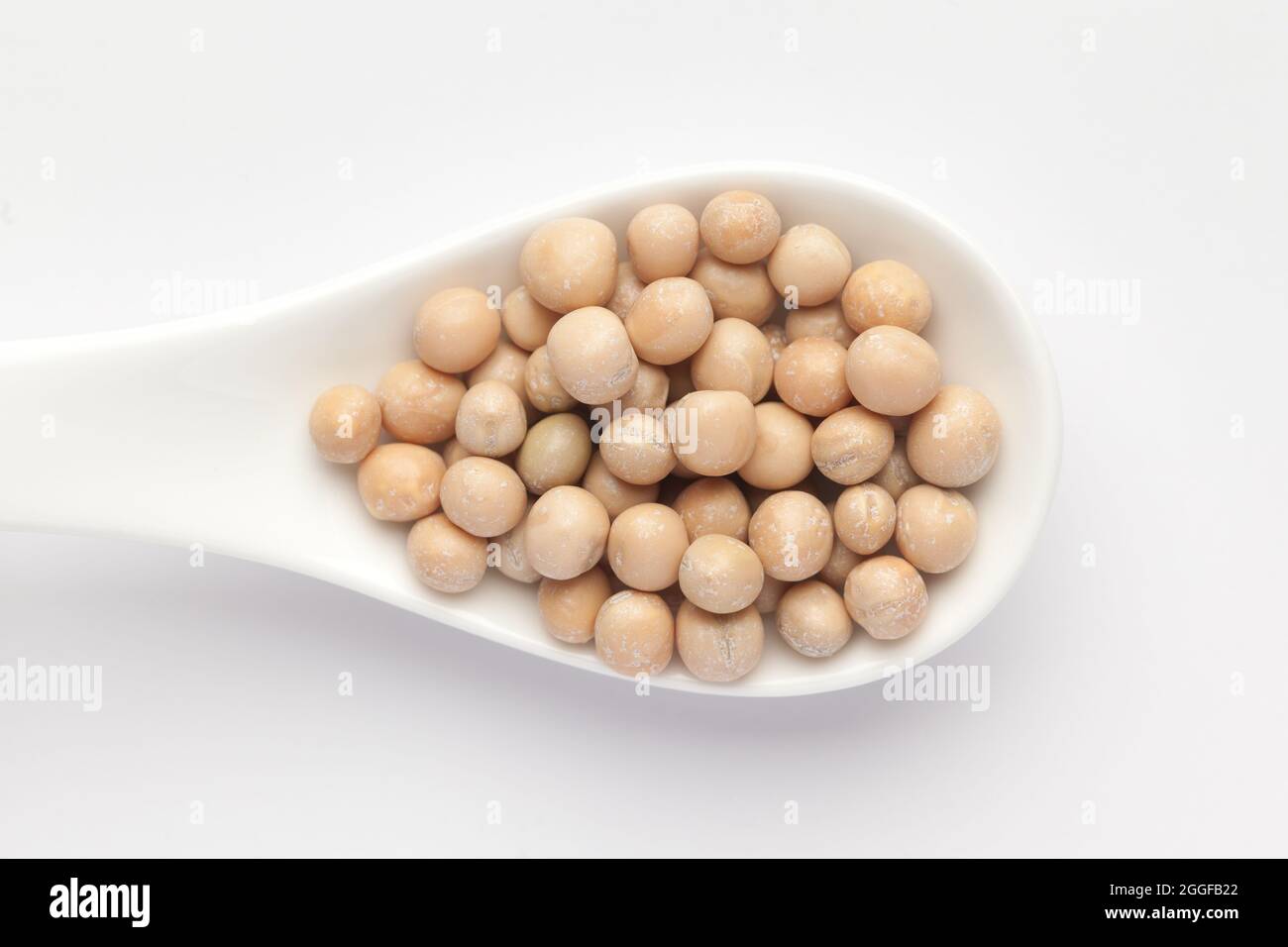 Macro primo piano di primo piano di piselli secchi organici interi (Pisum sativum) o matar dal su un cucchiaio per zuppa di ceramica bianca. Vista dall'alto Foto Stock